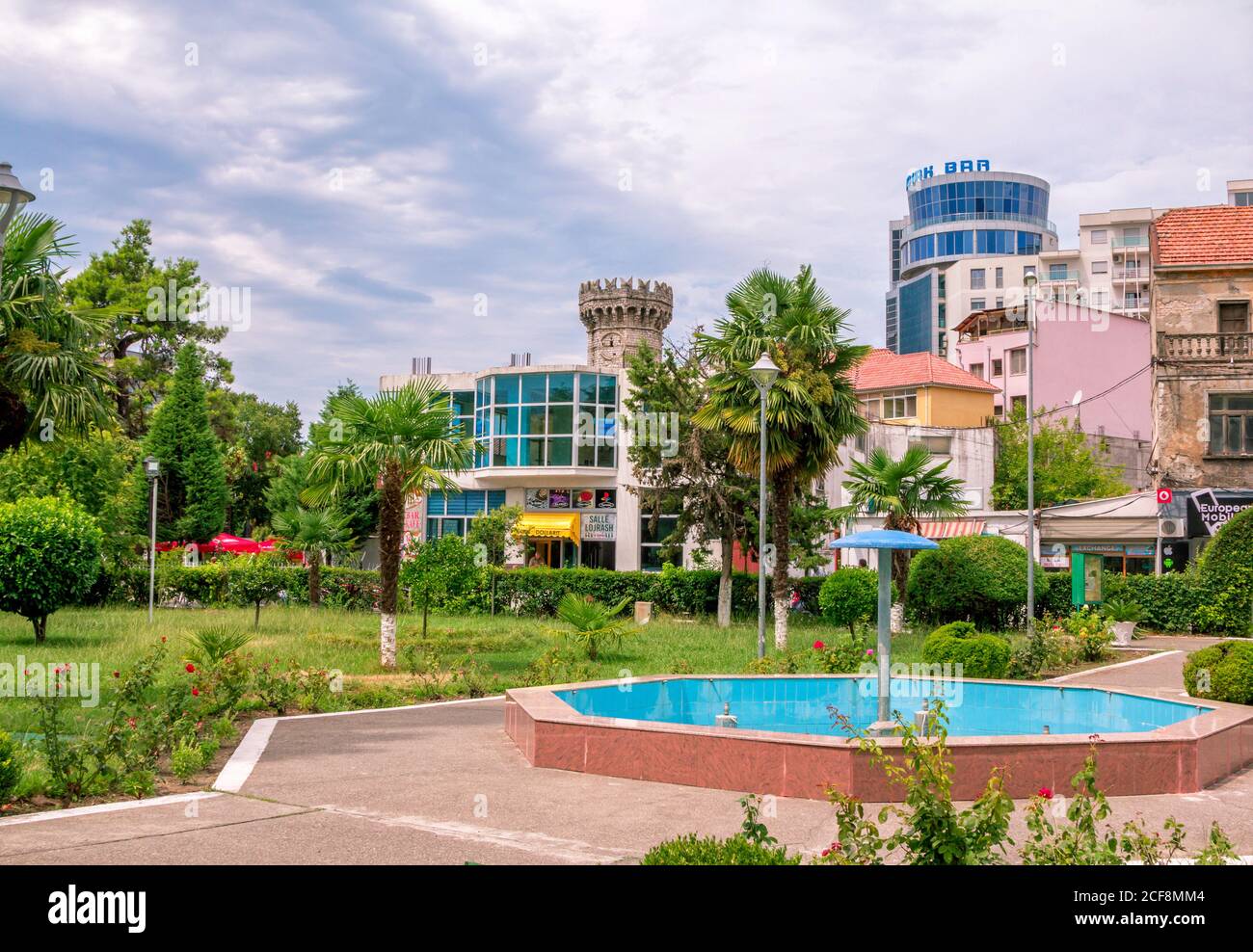 Shkoder oder oder Shkodra/Albanien – 8. August 2020: Sommerliche Stadtlandschaft – antike und moderne Gebäude, kleiner Garten mit Palmen, Sträuchern und grünen Rasenflächen Stockfoto