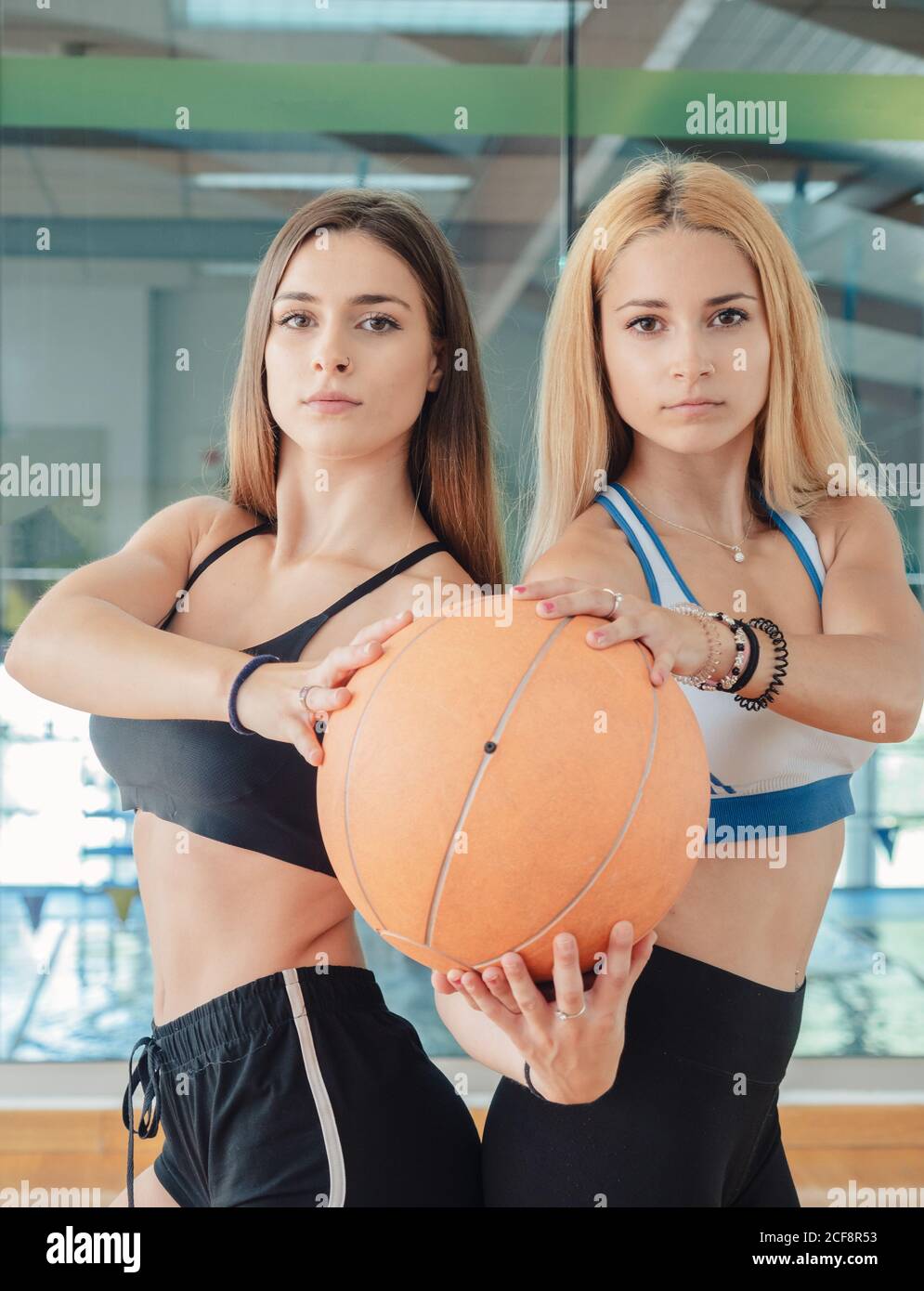 Seitenansicht von bestimmten schlanken Sportlerinnen dabei Kniebeugen beim Halten Medicine Ball zusammen Blick auf die Kamera in der Turnhalle Stockfoto