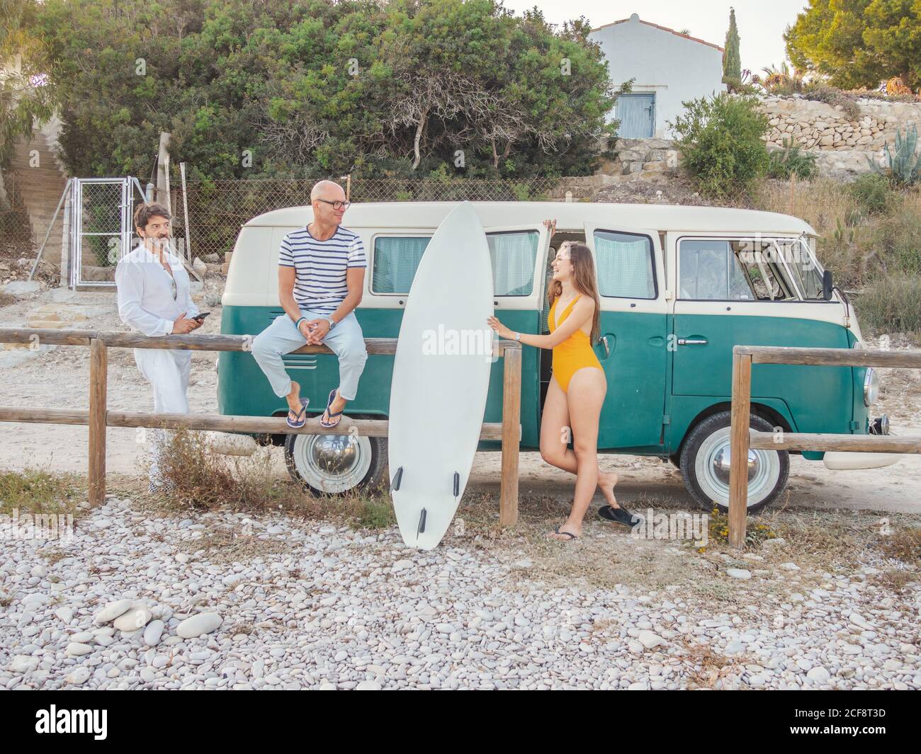 Aktive energetische Gay Familie mit Rest halten Surfbrett in der Nähe Anhänger Auf staubiger Straße auf dem Hintergrund der Landschaft Stockfoto