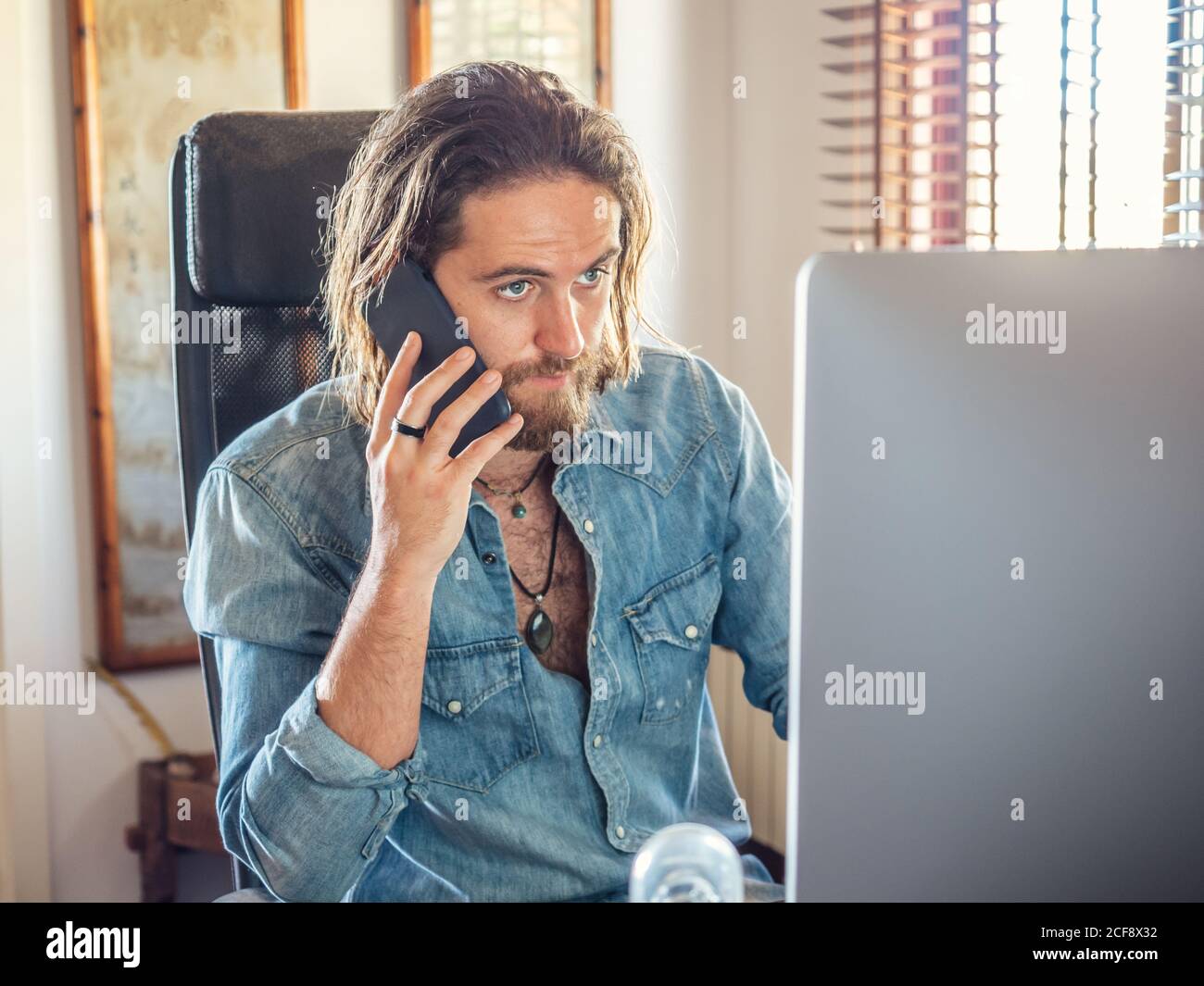 Aufmerksame männliche Surfen PC und sprechen auf mobilen in der Wohnung Stockfoto