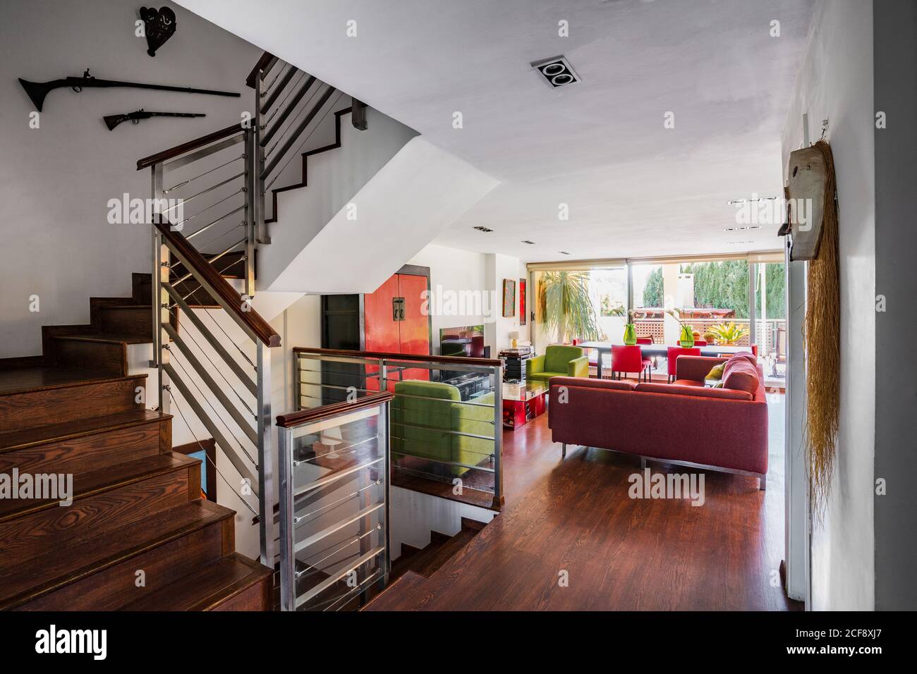 Modernes Wohnzimmer mit Holztreppe in rot und Grüne Farben mit großer Couch und Stühlen auf Laminat platziert Boden gegen weiße Wand Stockfoto