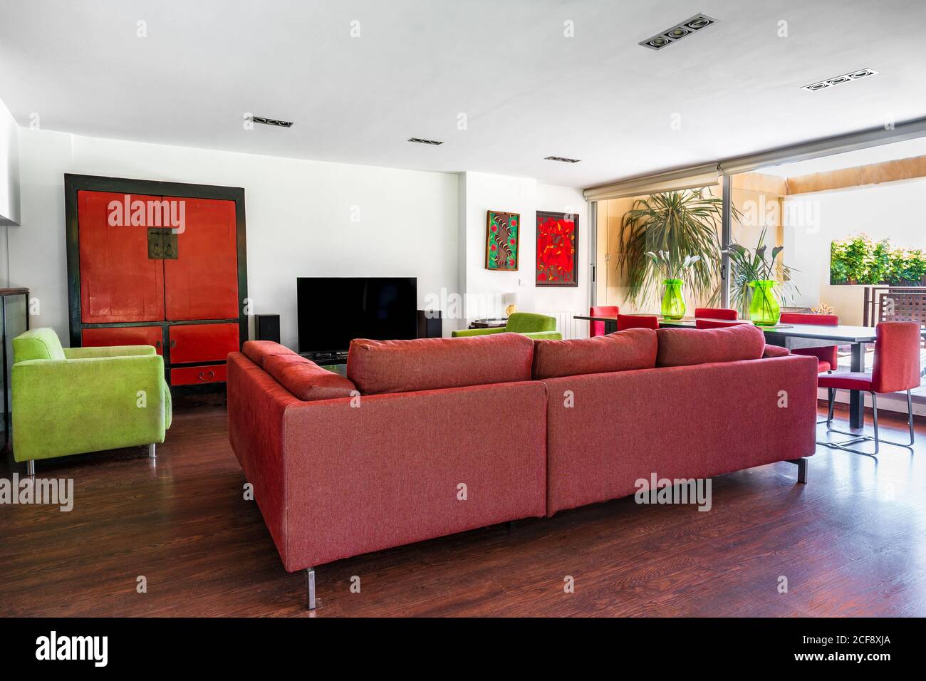 Moderne Wohnzimmereinrichtung in rot und grün mit Große Couch und Stühle auf Laminatboden gegen weiß platziert Wand Stockfoto