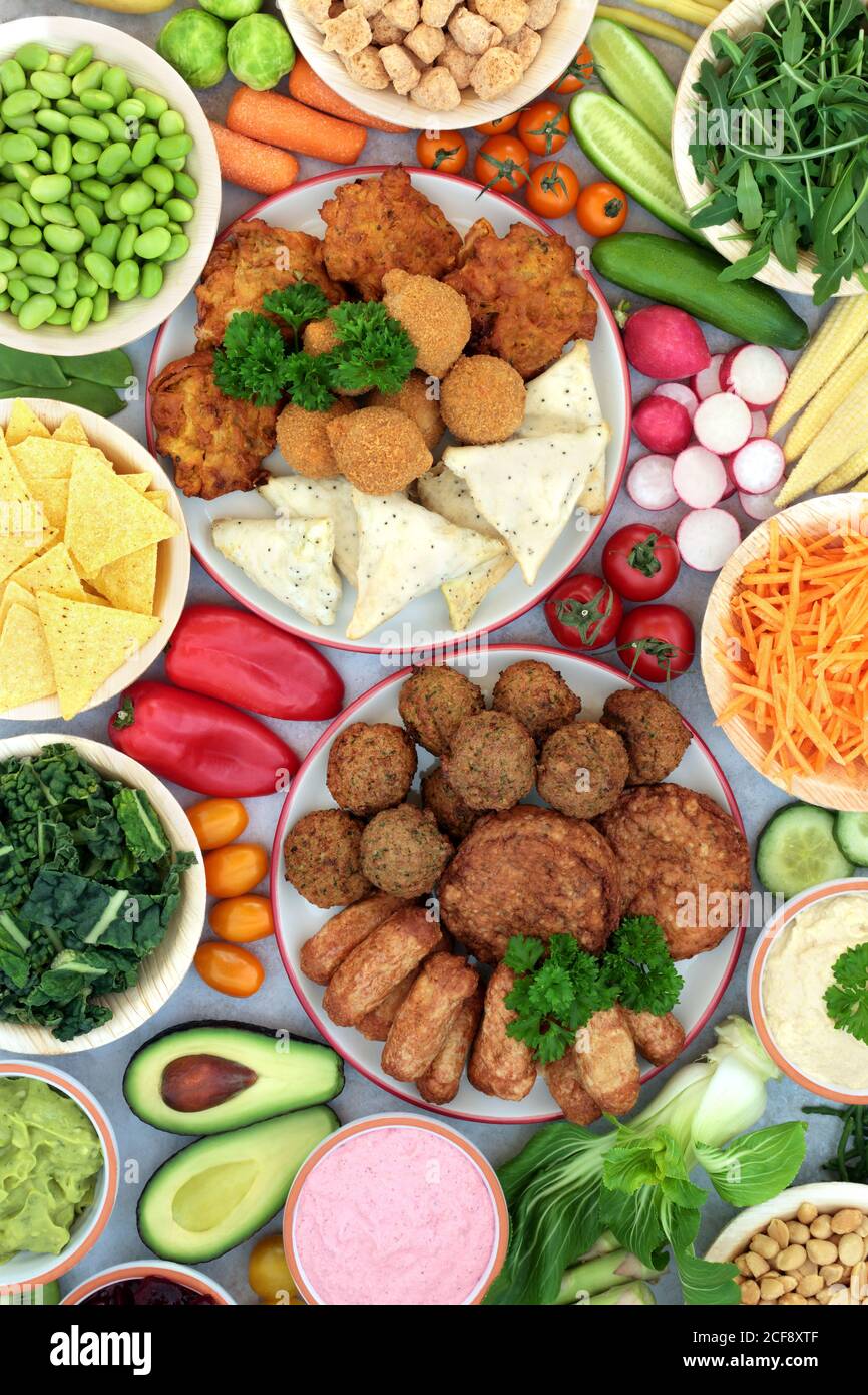 Gesundes Essen für eine nahrhafte vegane Ernährung, mit pflanzlichen Burgern, Würstchen, Bällen, Samosas & Zwiebel Bhajis mit Gemüse, Dips, Hülsenfrüchten & Snacks. Stockfoto