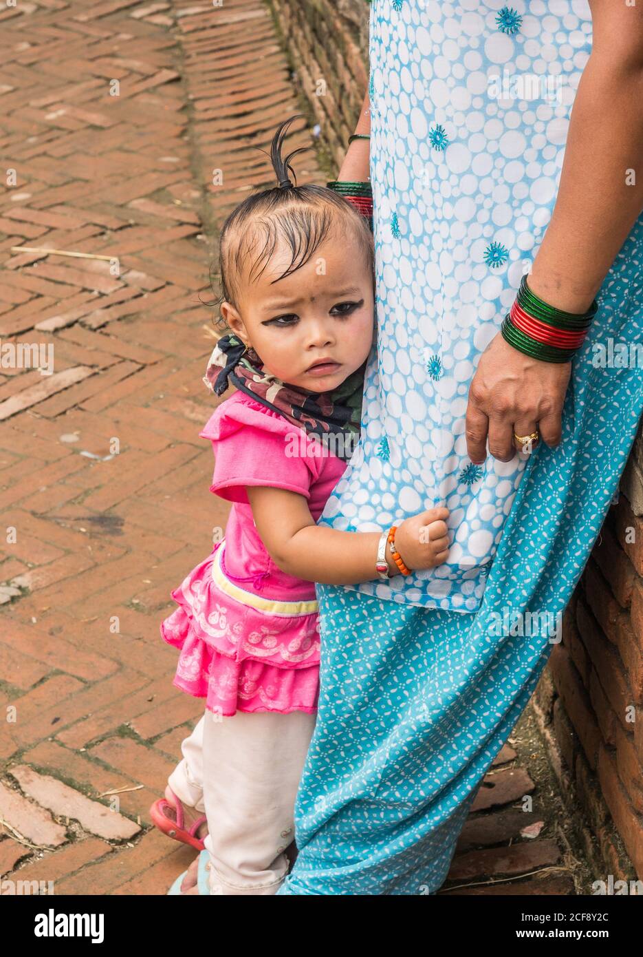 NEPAL, BHAKTAPUR - 19. AUGUST 2014: Seitenansicht eines kleinen ängstlichen indischen Kindes, das die Beine der Mutter auf der Straße hält Stockfoto