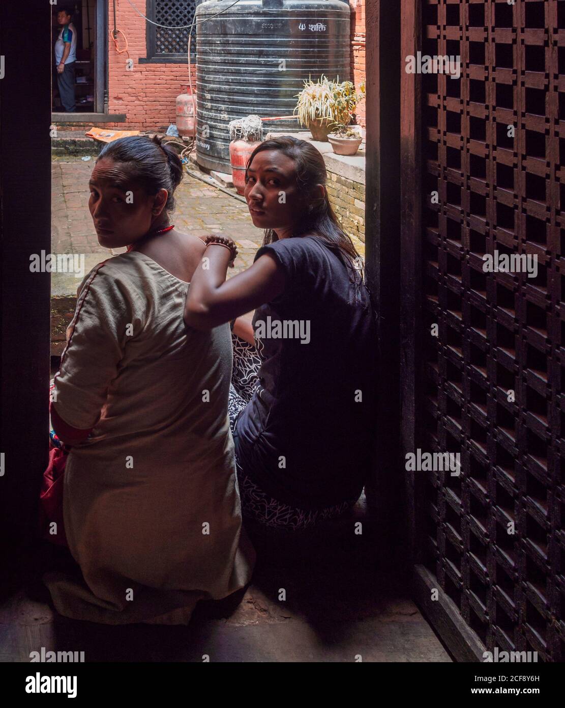 NEPAL, Kathmandu - 4. AUGUST 2014: Rückansicht von jungen Frauen, die auf dem Boden im Hof des Hauses ruhen und die Kamera betrachten Stockfoto
