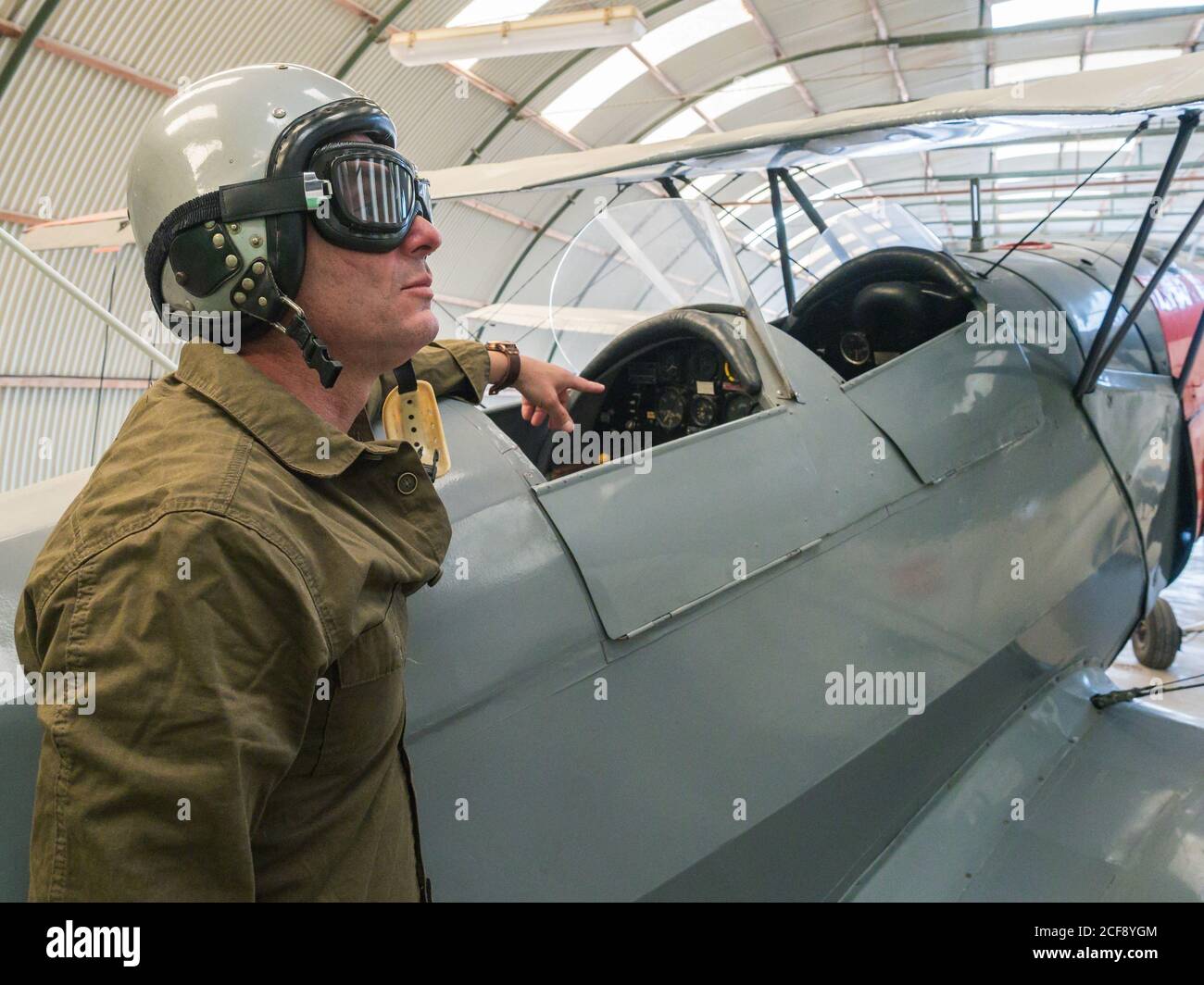 Seitenansicht des männlichen Piloten in der Ausrüstung, die neben dem Vintage steht Doppeldecker im hellen Hangar Stockfoto
