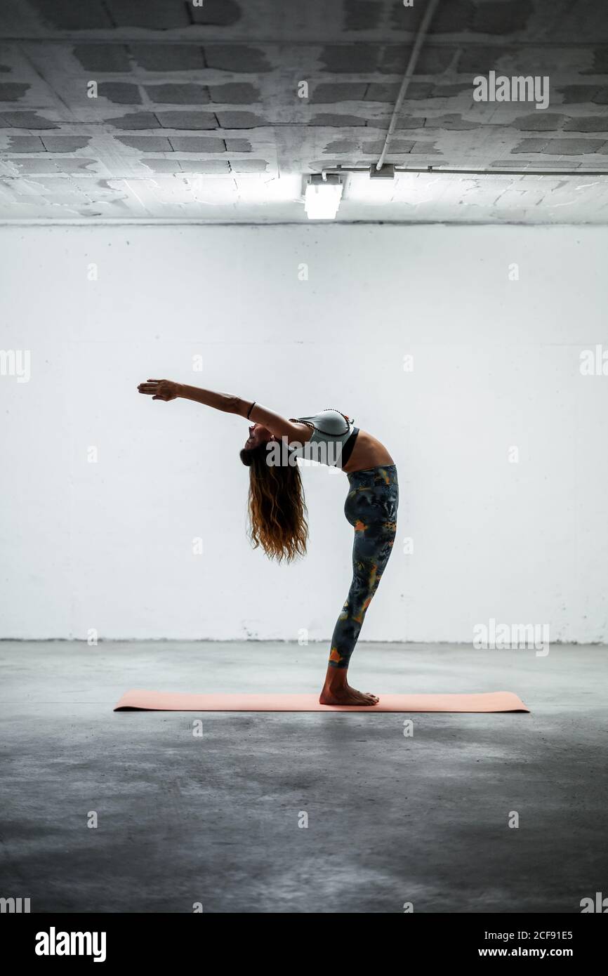 Seitenansicht einer ruhigen Frau mit Sport-Leggings und BH Balancing auf Bein im Stand backbend mit Gebet Hände und Suchen nach oben Stockfoto