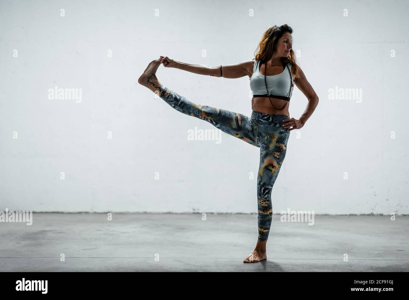 Frau in aktiver Kleidung, die barfuß auf Betonboden steht Hand an Toe Asana und wegschauen beim Balancieren auf Bein Stockfoto
