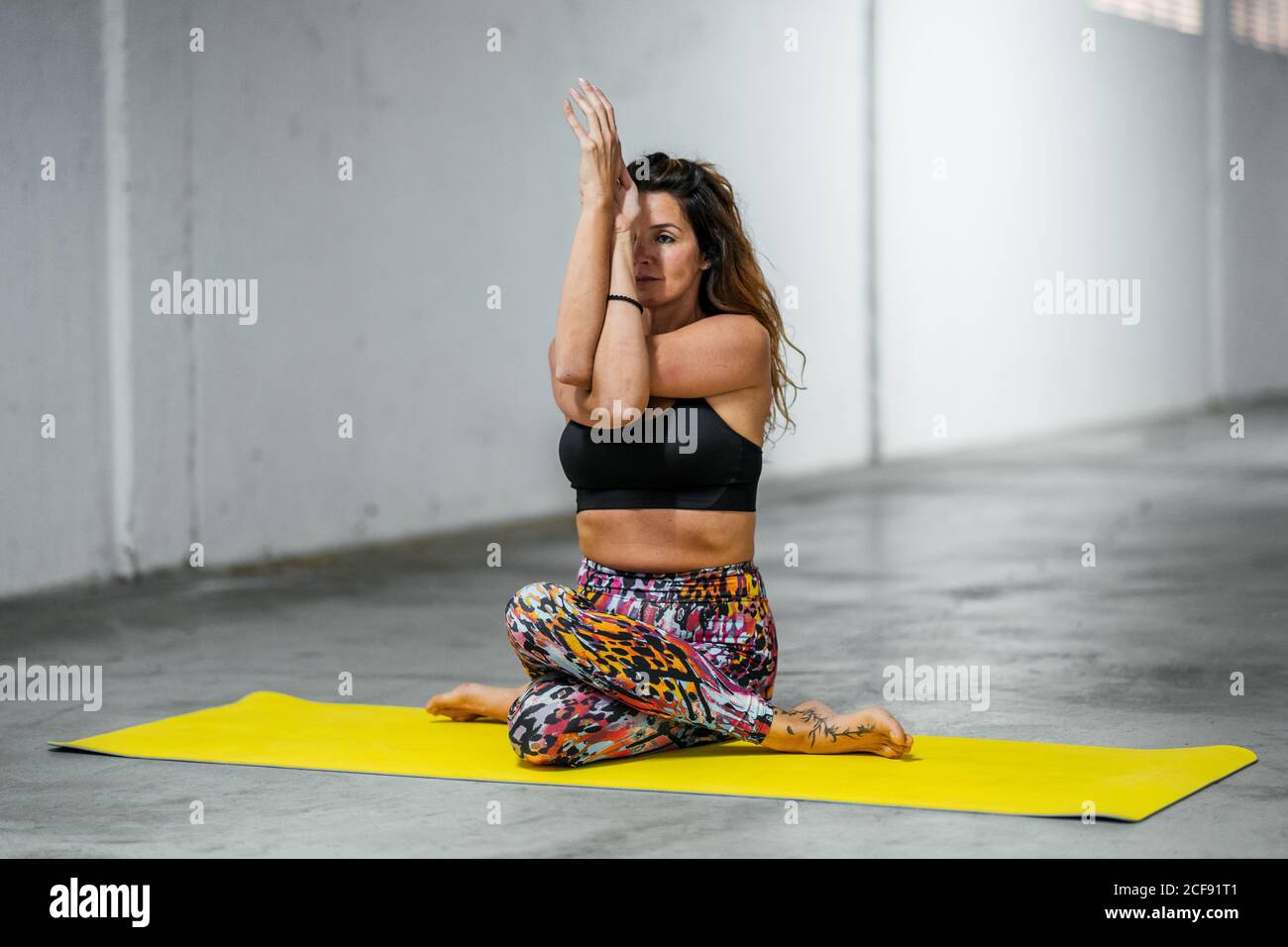Ruhig junge weiblich in Sportswear tun Kuh Gesicht Pose mit Adlerarme beim Yoga in der hellen Halle Stockfoto