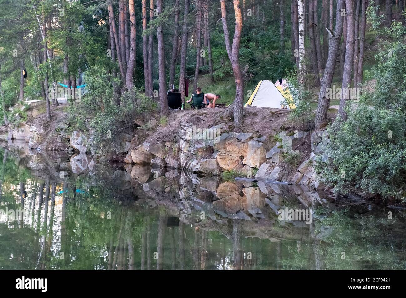 Camping am See. Blick auf touristische Zelte am Rande eines überfluteten Granitsteinbruchs zwischen Pinien Stockfoto