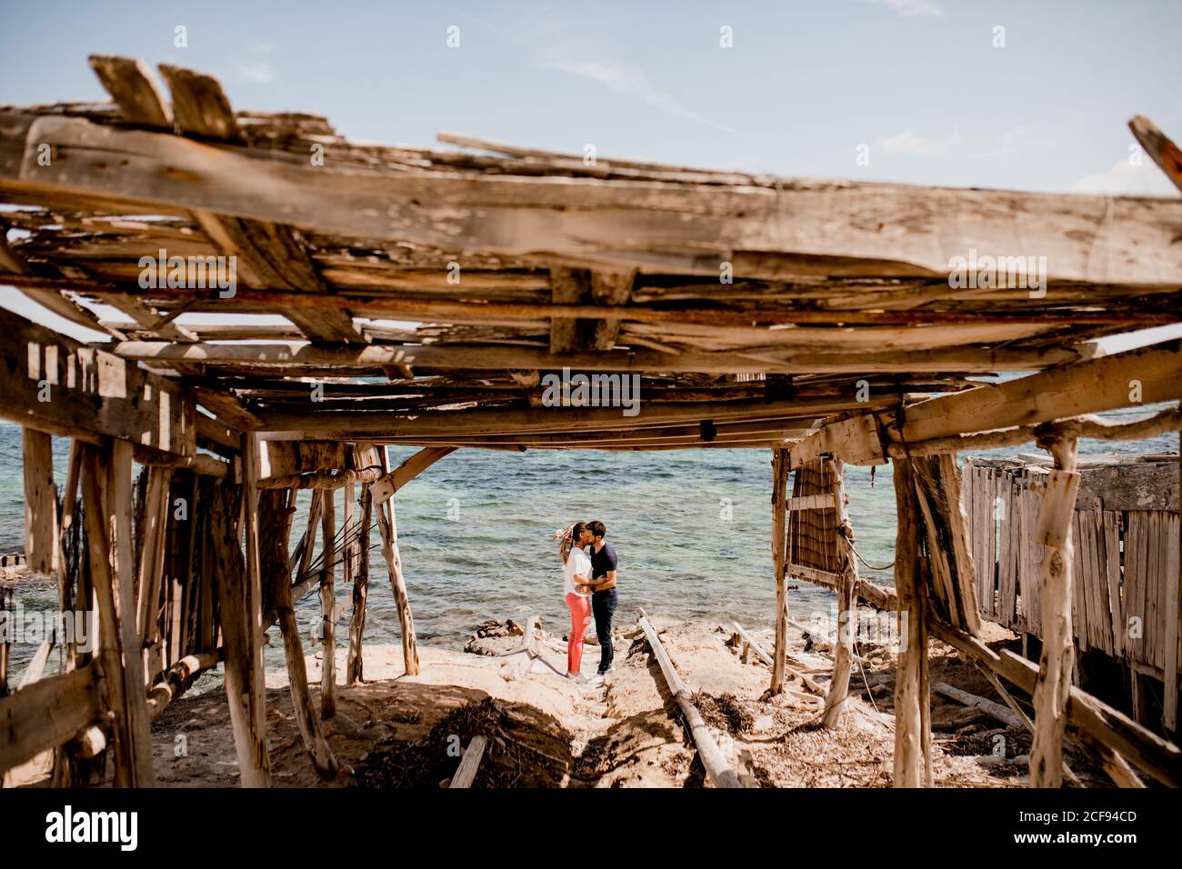 Seitenansicht eines romantischen Paares, das sich an der Küste in der Nähe von Holz umarmt Baldachin im Sommer Stockfoto