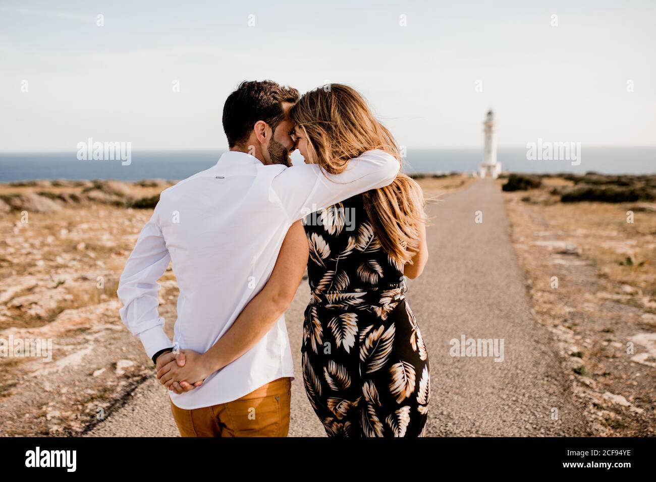Rückansicht des zarten Paares Umarmung auf Asphaltstraße zu Leuchtturm und Meeresküste im Sommer Stockfoto