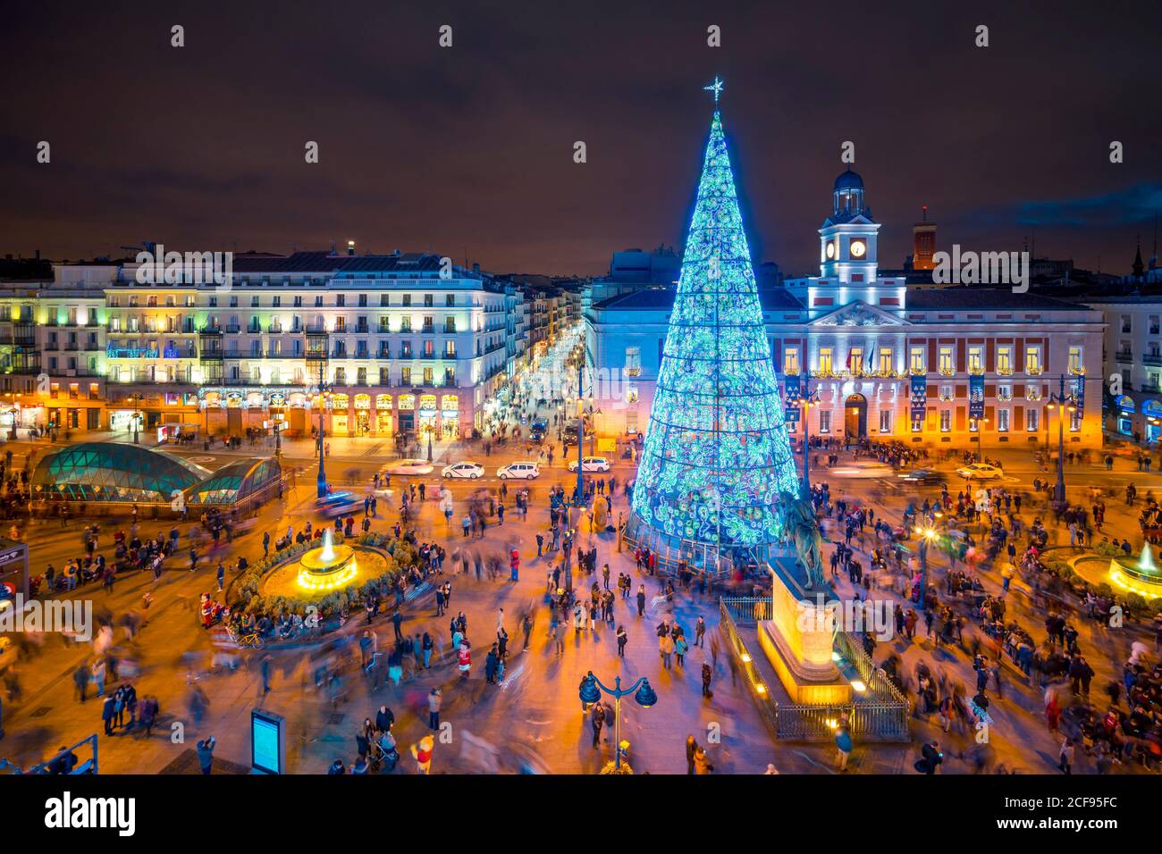 Madrid, Spanien - 19. Dezember 2018: Menschen genießen den Winterabend auf dem Stadtplatz Puerta de Sol mit geschmückten hohen leuchtenden Weihnachtsbaum mit blauen Lichtern und beleuchteten Gebäuden Stockfoto