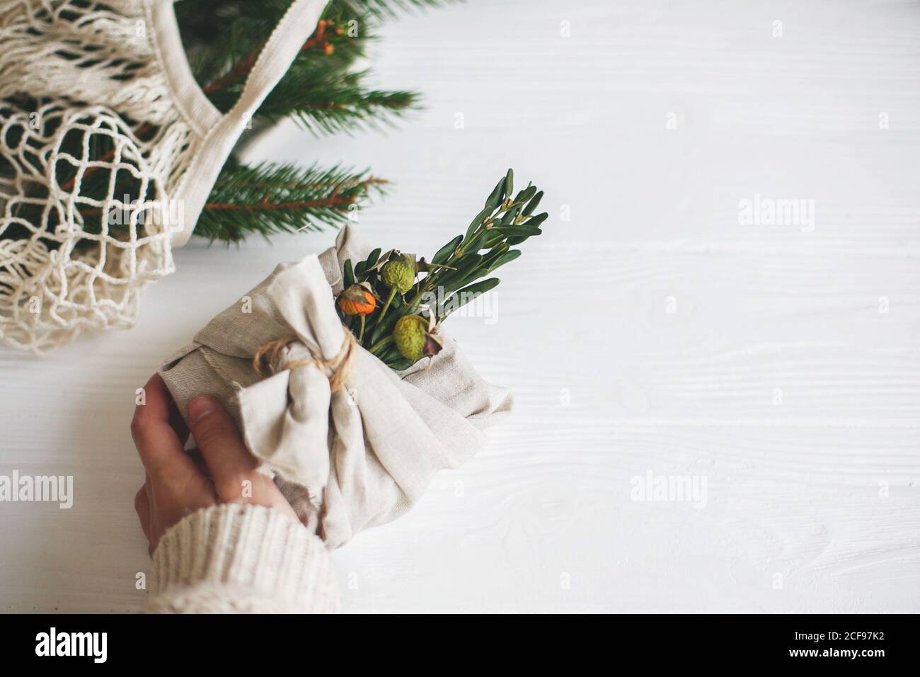 Weihnachtsferien ohne Verschwendung. Hand hält stilvolle weihnachtsgeschenk in Leinenstoff mit grünen Zweig auf rustikalen weißen Holzhintergrund eingewickelt. Sust Stockfoto