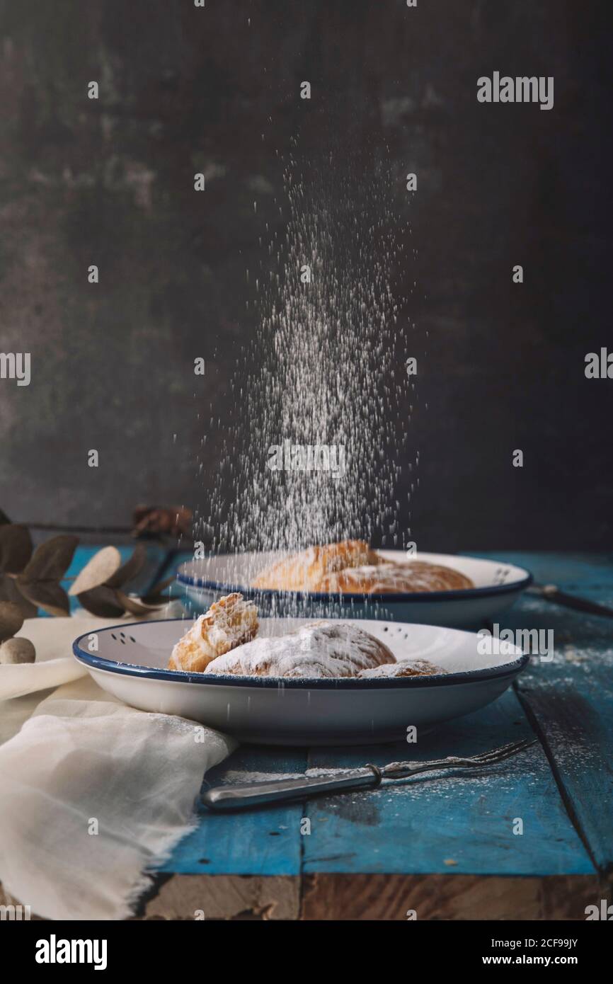 Puderzucker, der in ein köstliches Dessertbrot auf Blau fällt Tabelle Stockfoto