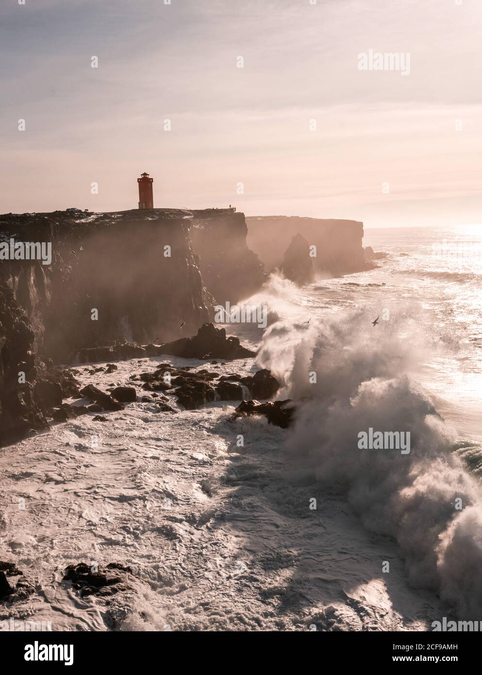 Sturmwellen an der Westküste Islands und Svörtuloft Leuchtturm in der Ferne Stockfoto
