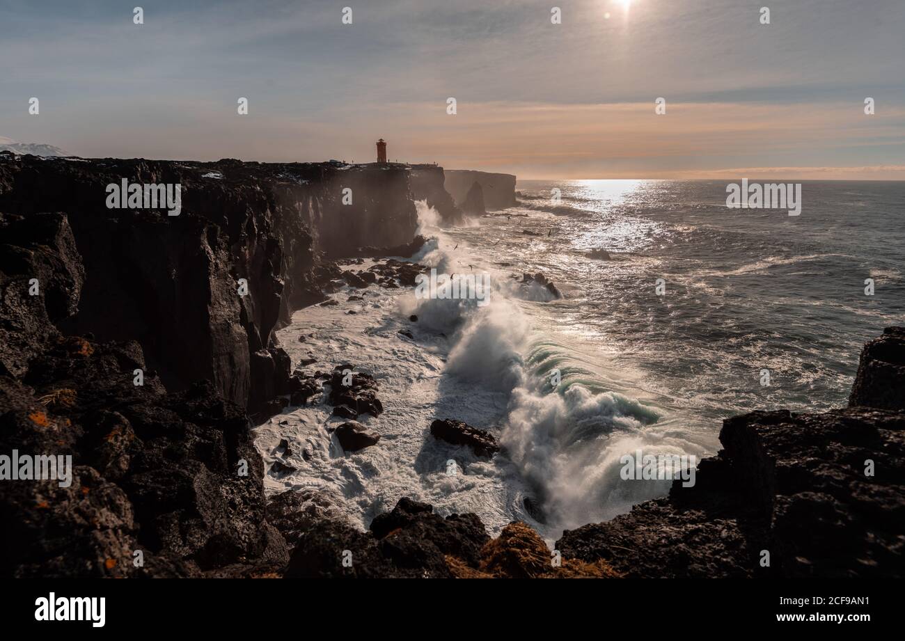 Sturmwellen an der Westküste Islands und Svörtuloft Leuchtturm in der Ferne Stockfoto