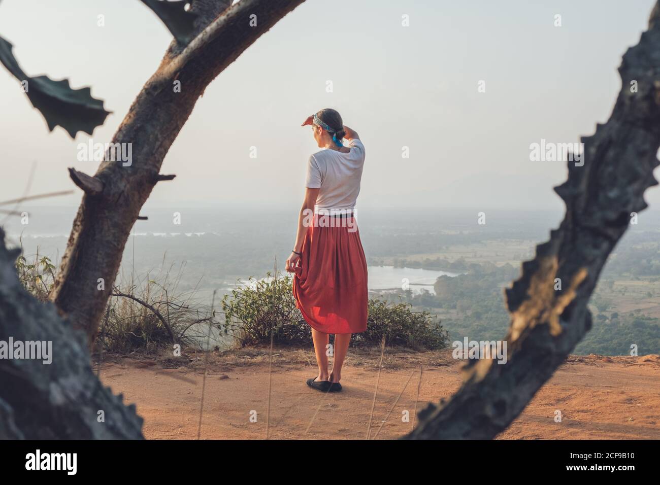 Rückansicht einer Frau in legerem T-Shirt und Rock, die auf einem sandigen Hügel steht und ihr Gesicht bedeckt, während sie den Sonnenuntergang genießt und durch Sri Lanka reist Stockfoto