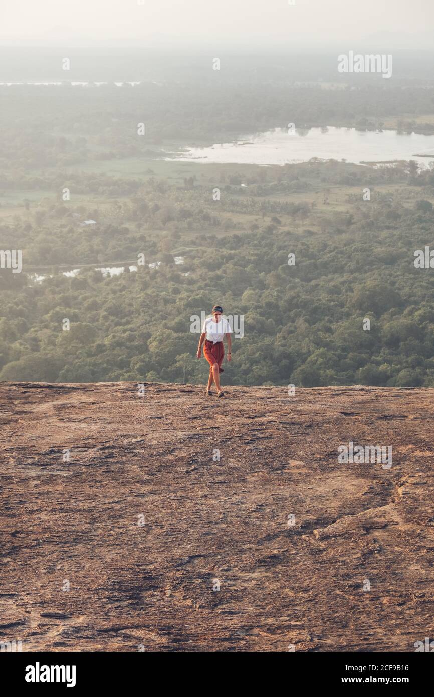 Von oben auf der Reise weiblich in legerer Kleidung bergauf laufen Auf dem Hintergrund des Tales mit Wald und See im Sommer Urlaub in Sigiriya Stockfoto