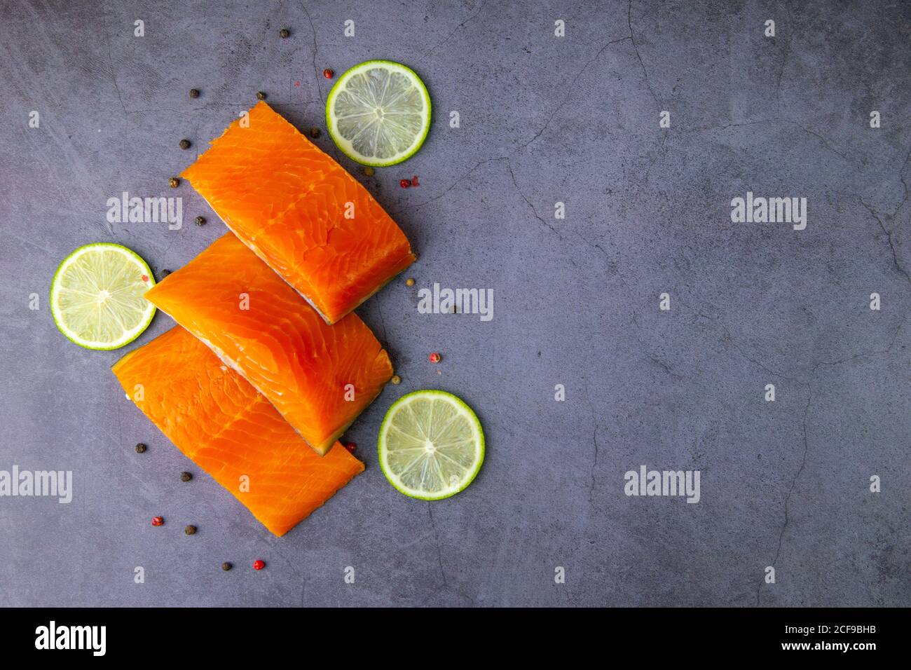 Drei Stück roher Lachs mit Gewürzen und Zitrone auf grauem Hintergrund. Gewürzte gesunde Lachsfilets ungekocht Stockfoto