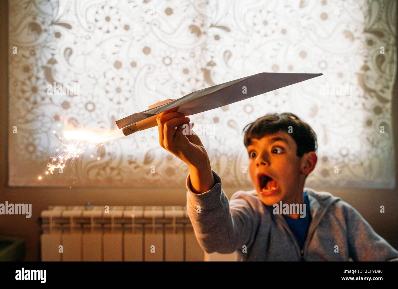 Amüsiert Junge spielt mit Papier Flugzeug mit Petard im Zimmer Stockfoto