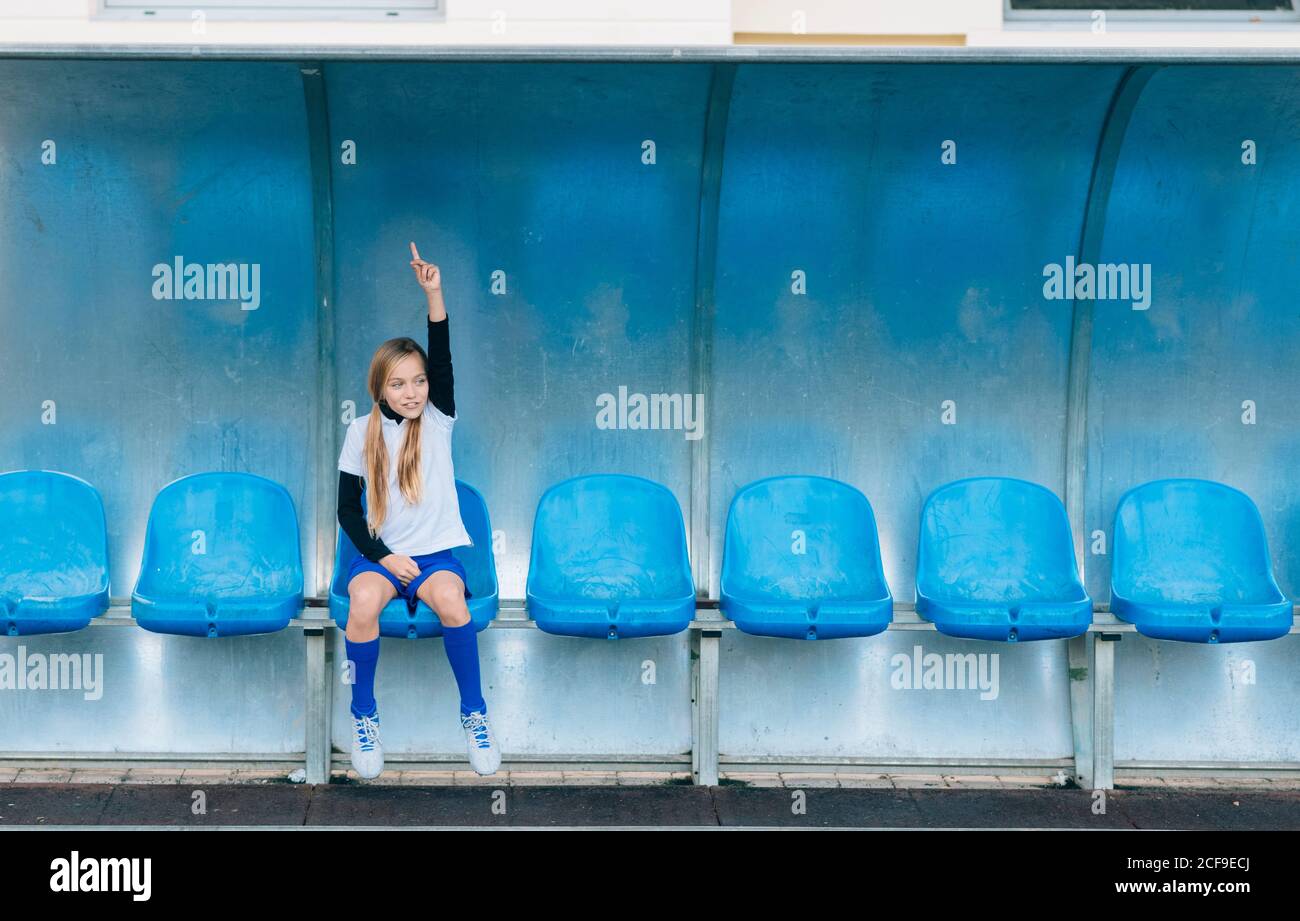 Mädchen in Fußballuniform allein auf blauem Plastiksitz sitzen Nach Spielversagen im Sportverein Stockfoto