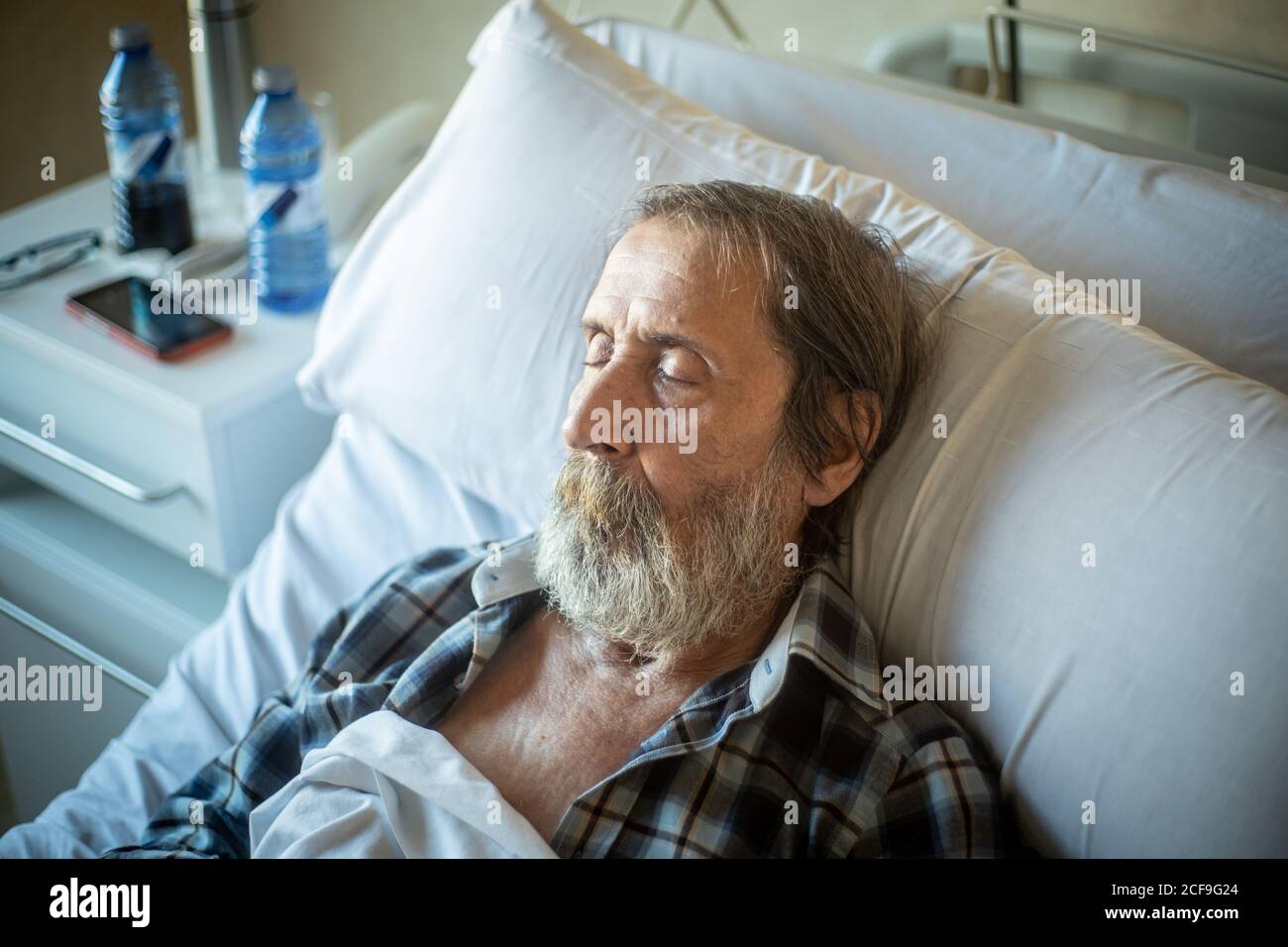 Ruhiger alter Mann mit Bart unter der Decke auf dem Bett liegen In der Krankenstation und schlafen Stockfoto