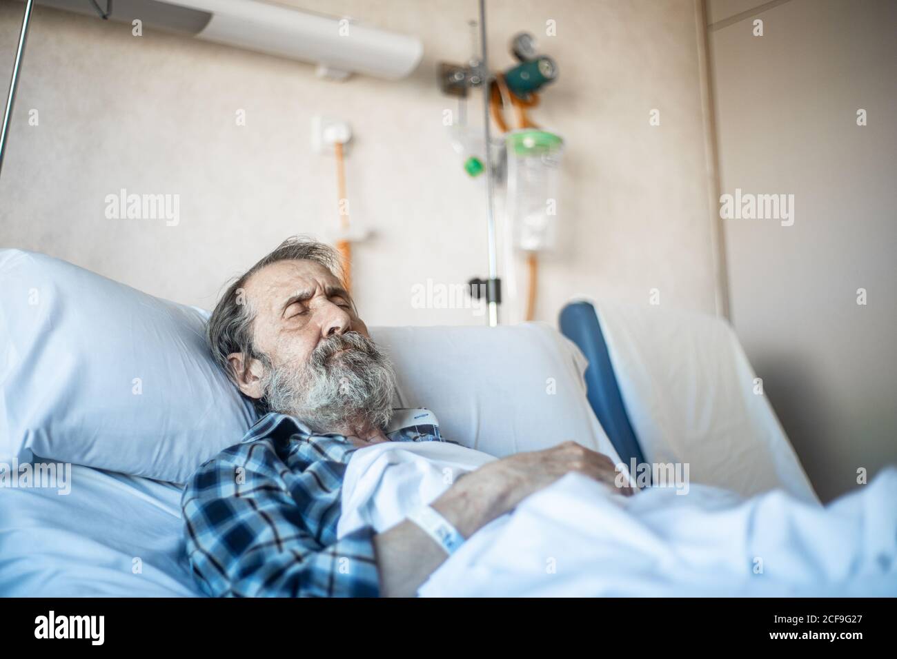 Ruhiger alter Mann mit Bart unter der Decke auf dem Bett liegen In der Krankenstation und schlafen Stockfoto