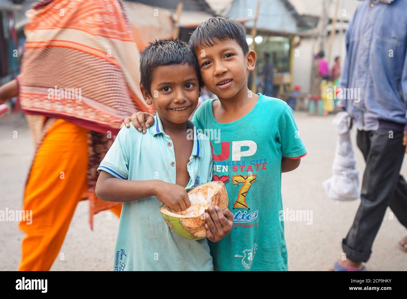 Bangladesch - Januar 19 2019: Kleiner Junge umarmt fröhlichen Bruder mit Kokosnuss, während er auf einer überfüllten Stadtstraße steht Stockfoto