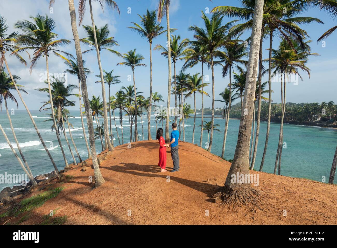 Seitenansicht der ruhigen paar Reisende in legerer Kleidung stehend Und die Hände am tropischen Hügel mit Palmen in der Nähe halten Blaues Meer Stockfoto