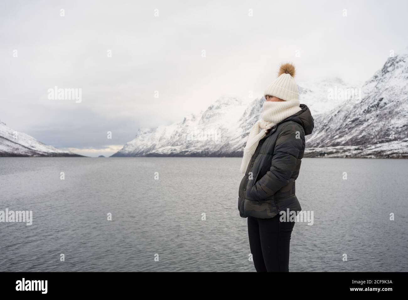 Glückliche Frau mit erstaunlichen Augen mit schwarzer Jacke und bedeckt Weißer warmer Hut und Schal, der gegen Weiß absieht, verschwommen Hintergrund in Norwegen Stockfoto