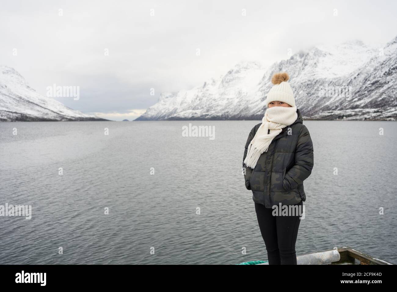 Glückliche Frau mit erstaunlichen Augen mit schwarzer Jacke und bedeckt Weißer warmer Hut und Schal, der die Kamera gegen Weiß anschaut Verschwommener Hintergrund in Norwegen Stockfoto
