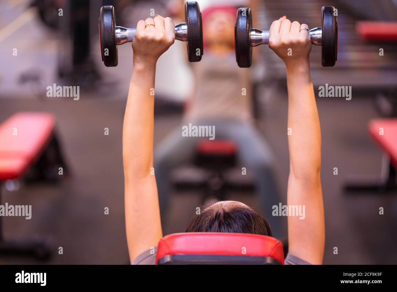 Rückansicht der nicht erkennbaren starken Sportlerin im Sportbekleidungssport Hanteln drücken auf die Schrägbank im modernen Fitnesscenter Stockfoto