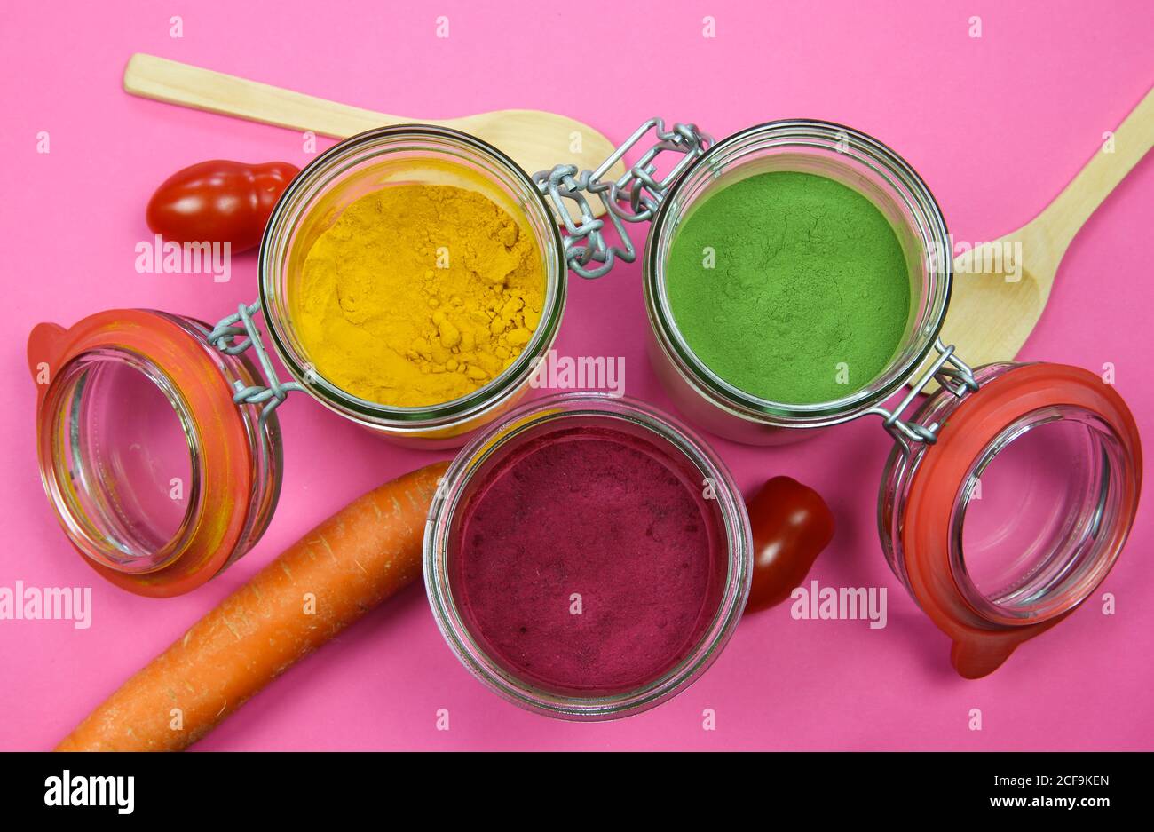 Draufsicht auf isolierte Einmachgläser und Holzlöffel mit gelbem Kurkuma, roter Rote Bete und grünem Spinatpulver, rosa Hintergrund. Stockfoto