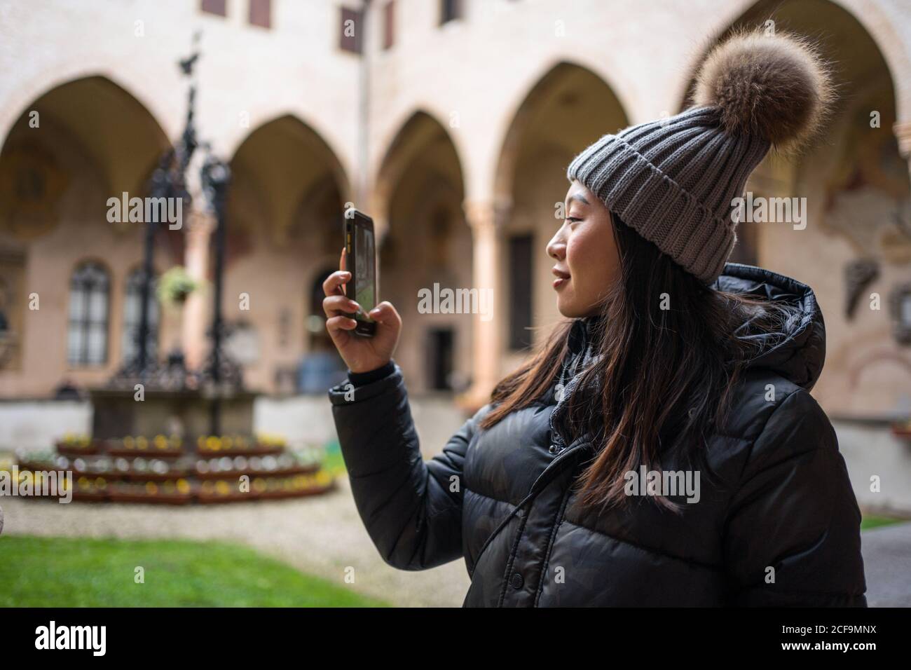 Seitenansicht der asiatischen weiblichen Touristen in warmer Kleidung und hat fotografieren auf dem Handy, während Sie die alte Basilika erkunden Von San Antonio in Padova in Italien Stockfoto