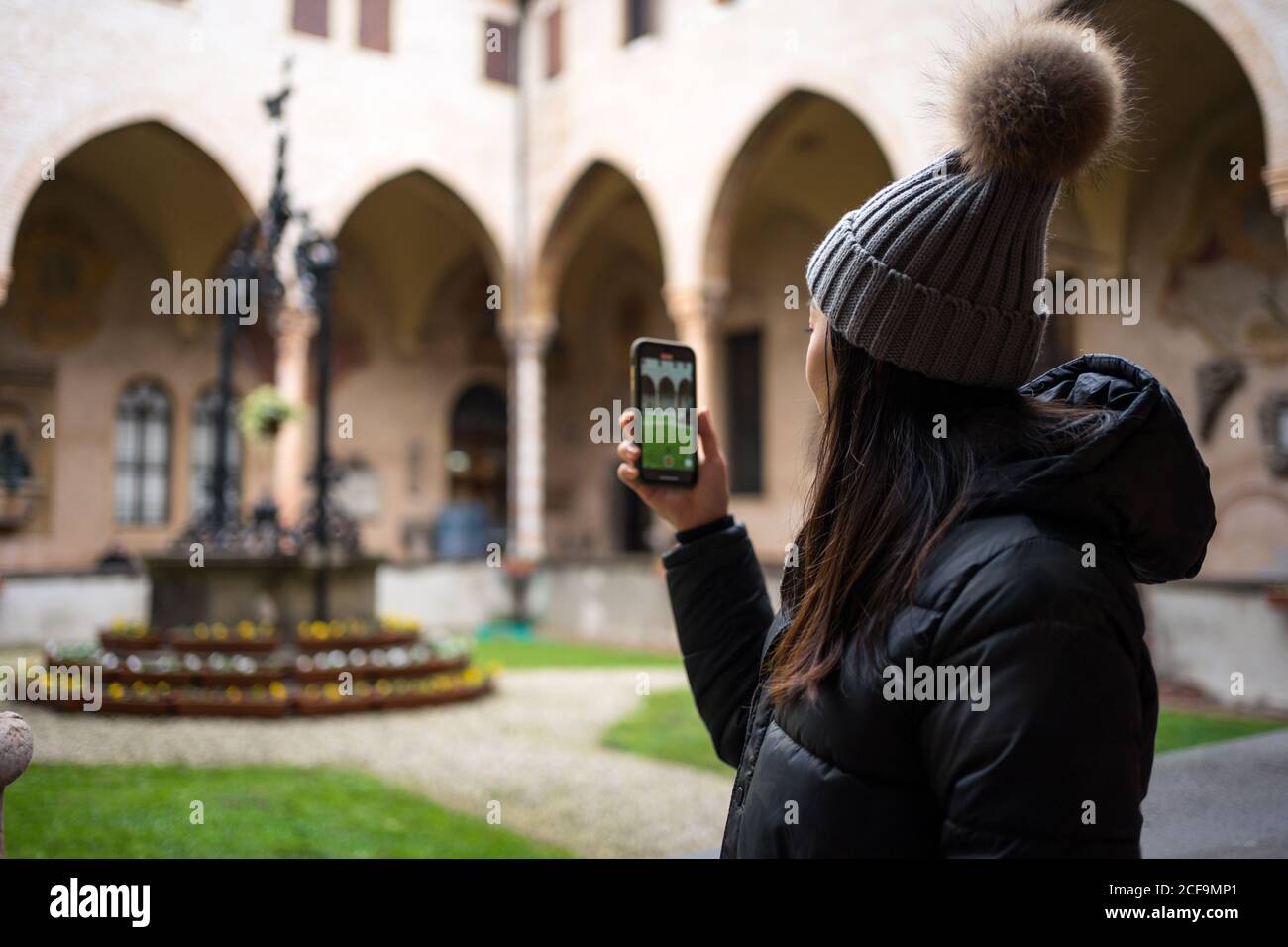 Seitenansicht der asiatischen weiblichen Touristen in warmer Kleidung und hat fotografieren auf dem Handy, während Sie die alte Basilika erkunden Von San Antonio in Padova in Italien Stockfoto