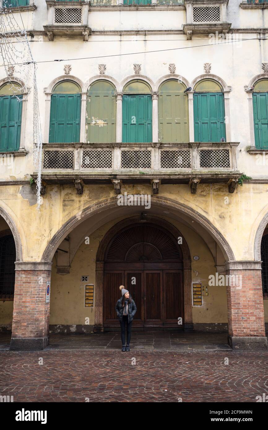 Frau im Urlaub in warmer Kleidung und Hut steht auf Block Steinstraße mit alten bunten Gebäude mit Bogen an Padua in Italien Stockfoto