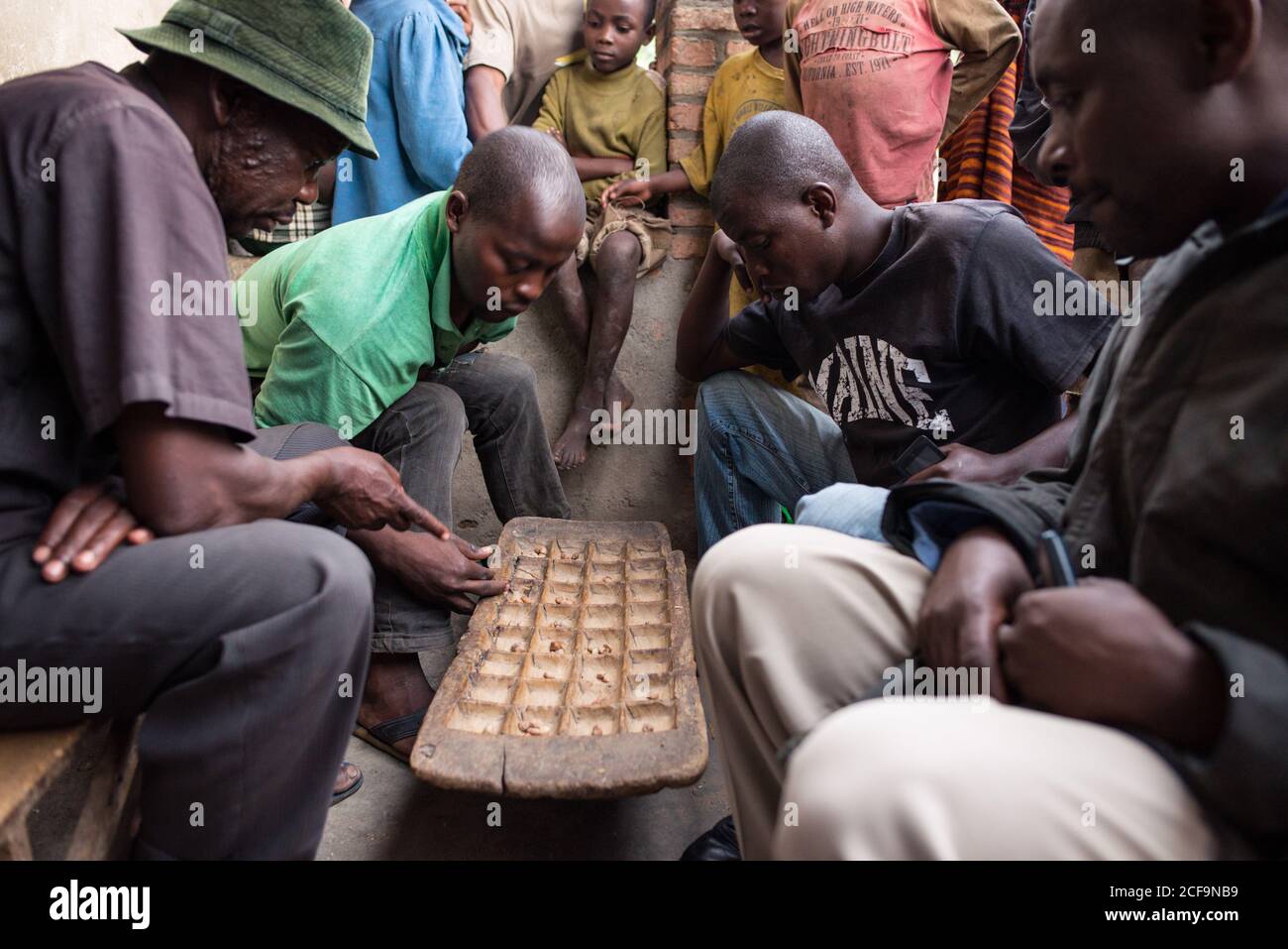 Ruanda, Afrika - 14. Dezember 2019: Gruppe von fokussierten afrikanischen Männern spielen Brettspiel auf der Straße im Dorf sitzen Stockfoto