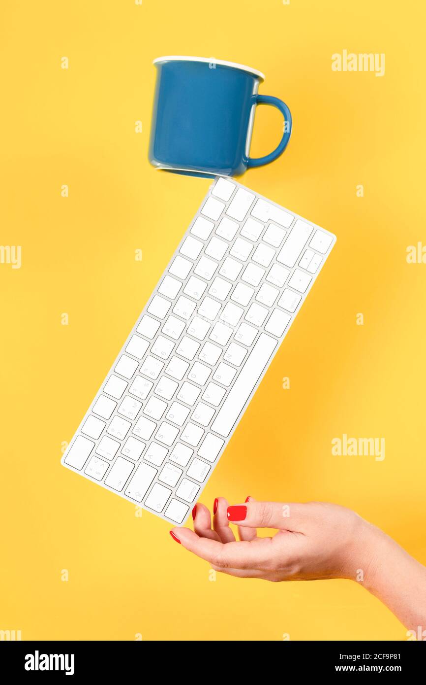 Tastatur und Tasse Kaffee Waagen auf der Hand der Frau auf Gelber Hintergrund Stockfoto