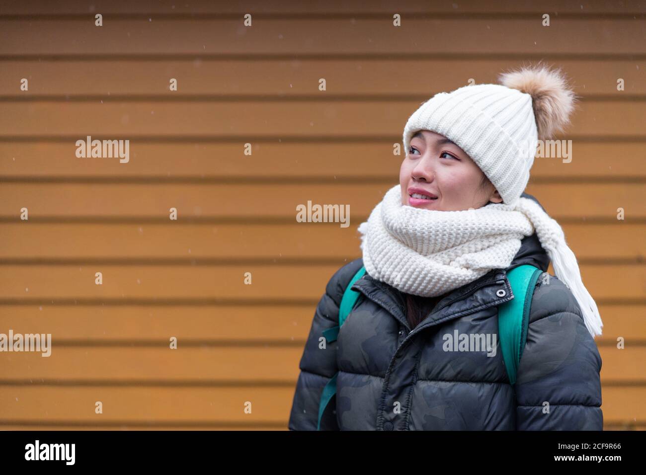Neugierige asiatische weibliche Reisende in warmer Kleidung und Hut stehen Und mit der hölzernen Wand des Hauses auf verschwommen wegschauen Hintergrund bei Tromso in Norwegen Stockfoto