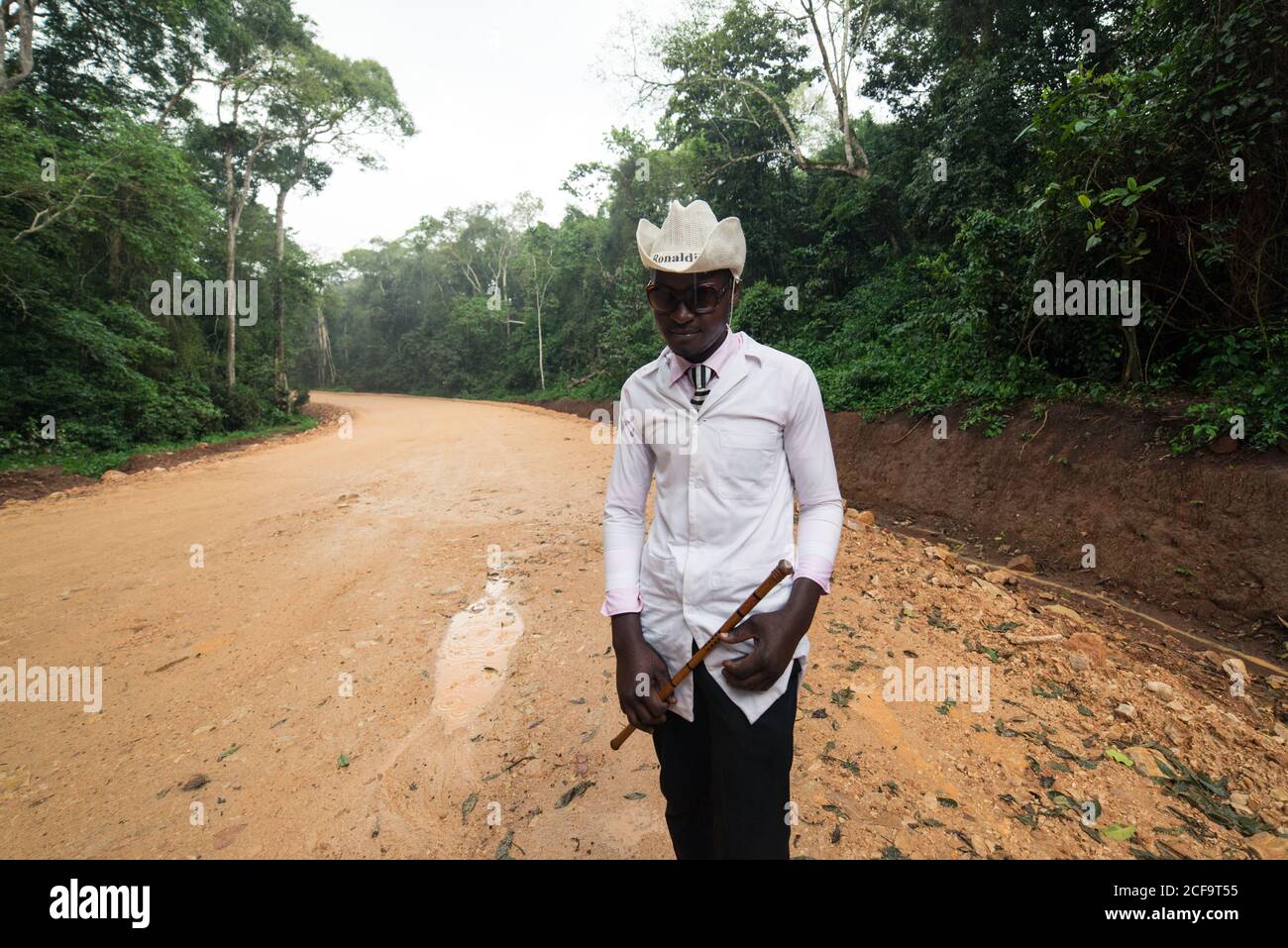 Uganda - November, 26 2016: Freundlicher, reifer schwarzer Mann, gut gekleidet mit Cowboyhut, der die Kamera anschaut, während er auf der Feldweg-Straße im Dorf steht Stockfoto