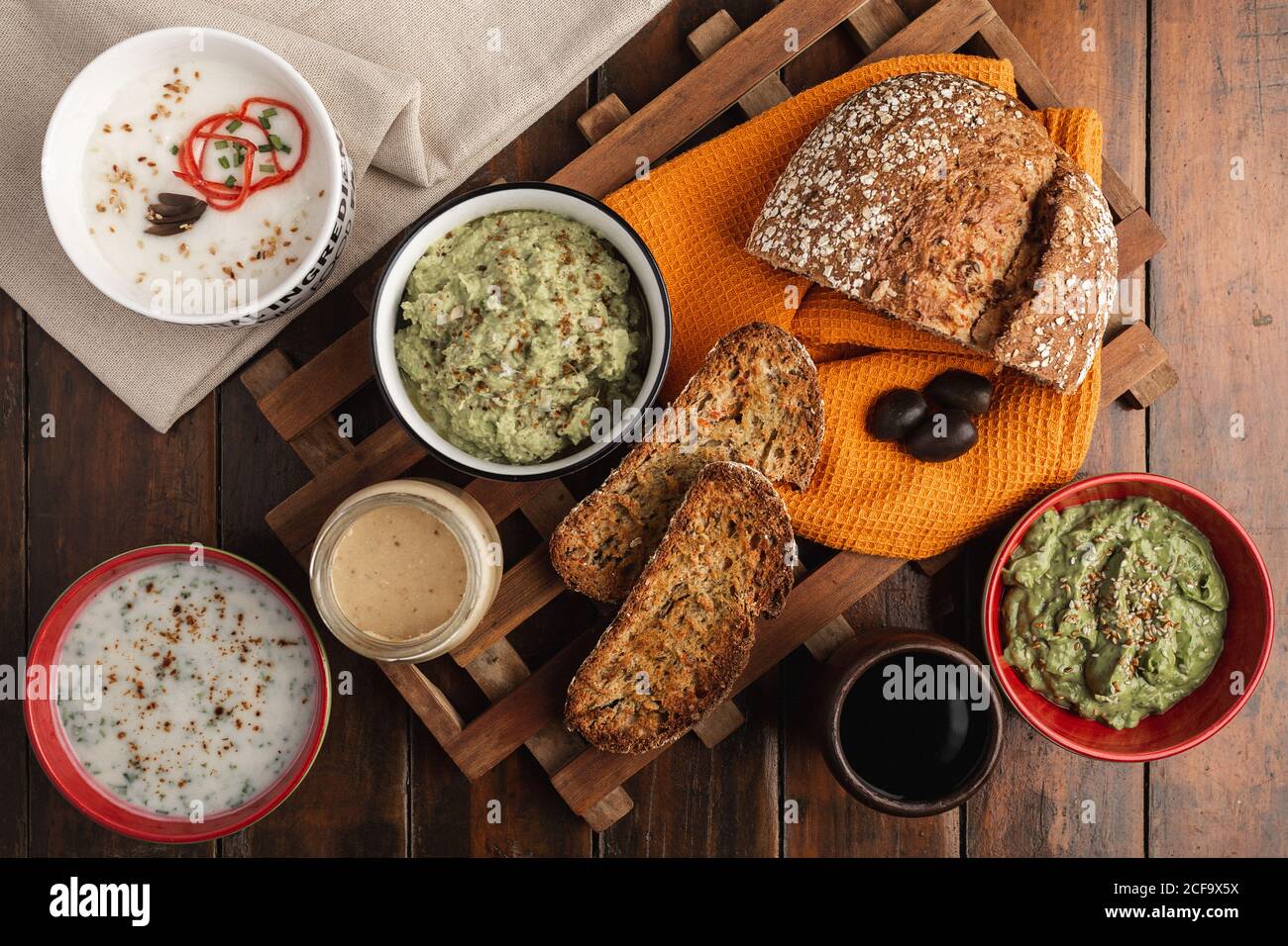 Von oben appetitlich verschiedene Saucen in rot-weißen Schalen mit Sesamkerne Belag und in Scheiben geröstetes, duftendes, frisch gebackenes Brot Auf Holzoberfläche Stockfoto