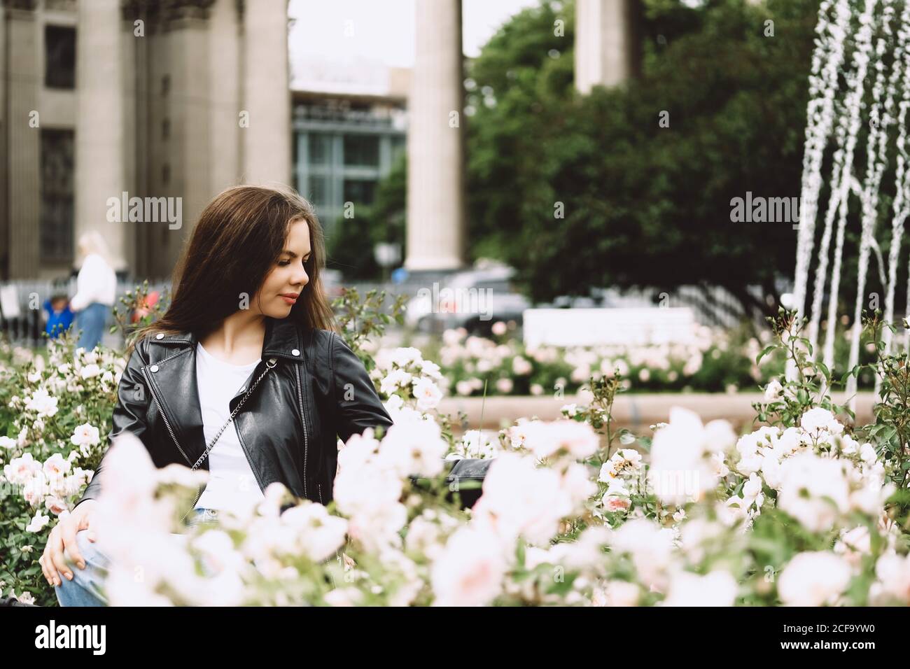 Junge Frau mit langen Haaren in der Straße einer Großstadt, umgeben von Rosen. Sankt Petersburg, Russland. Stockfoto