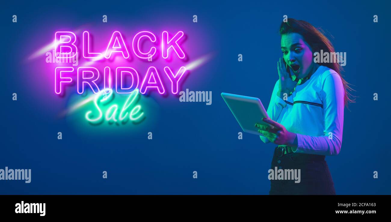 Erstaunt. Porträt einer jungen Frau in Neon auf blauem Studiohintergund. Menschliche Emotionen, Black friday, Cyber monday, Käufe, Verkäufe, Finanzierungskonzept. Copyspace. Nahtlose Post für instagram. Stockfoto