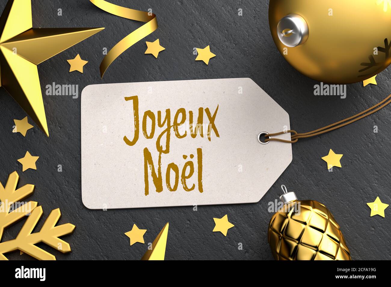 Weihnachten - Geschenk-Tag mit der französischen Frohen Weihnachtsbotschaft 'Joyeux Noël' auf schwarzem Steingrund mit goldfarbenen weihnachtsornamenten. Stockfoto