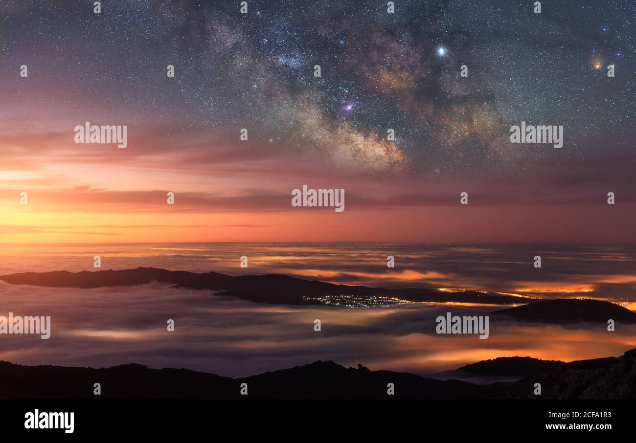 Drone Blick auf atemberaubende bunte Dämmerung über dunklen Berg scheint Spitzen in Wolken unter Licht von Sternenlicht in dunkler Nacht Himmel Stockfoto
