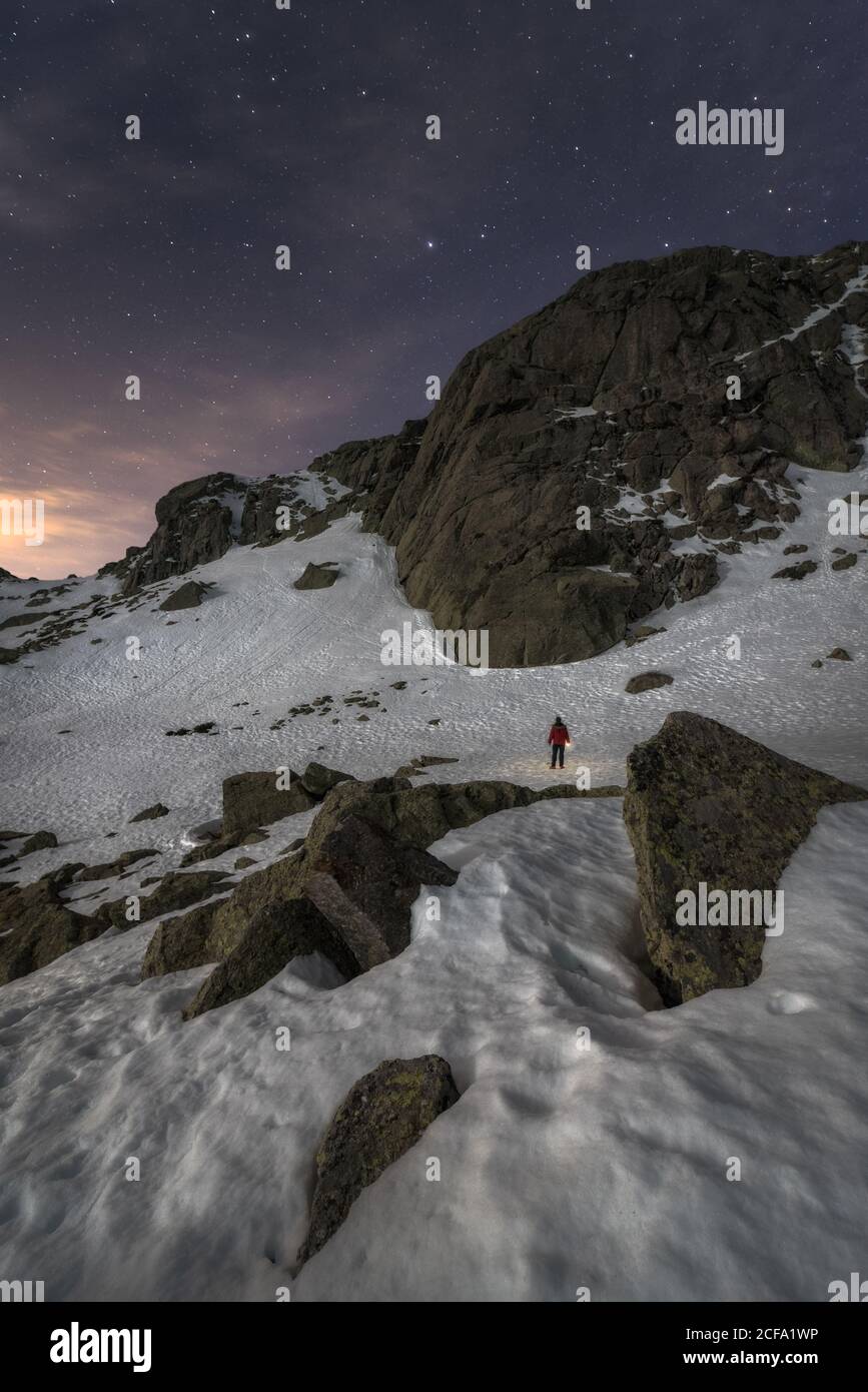 Entfernte Silhouette des Reisenden stehend auf mit reinem Weiß bedeckt Schnee grobe Bergkette lokalisieren im Hintergrund der Dämmerung scheint Sterne dunkel blau Nachthimmel im Winter Stockfoto