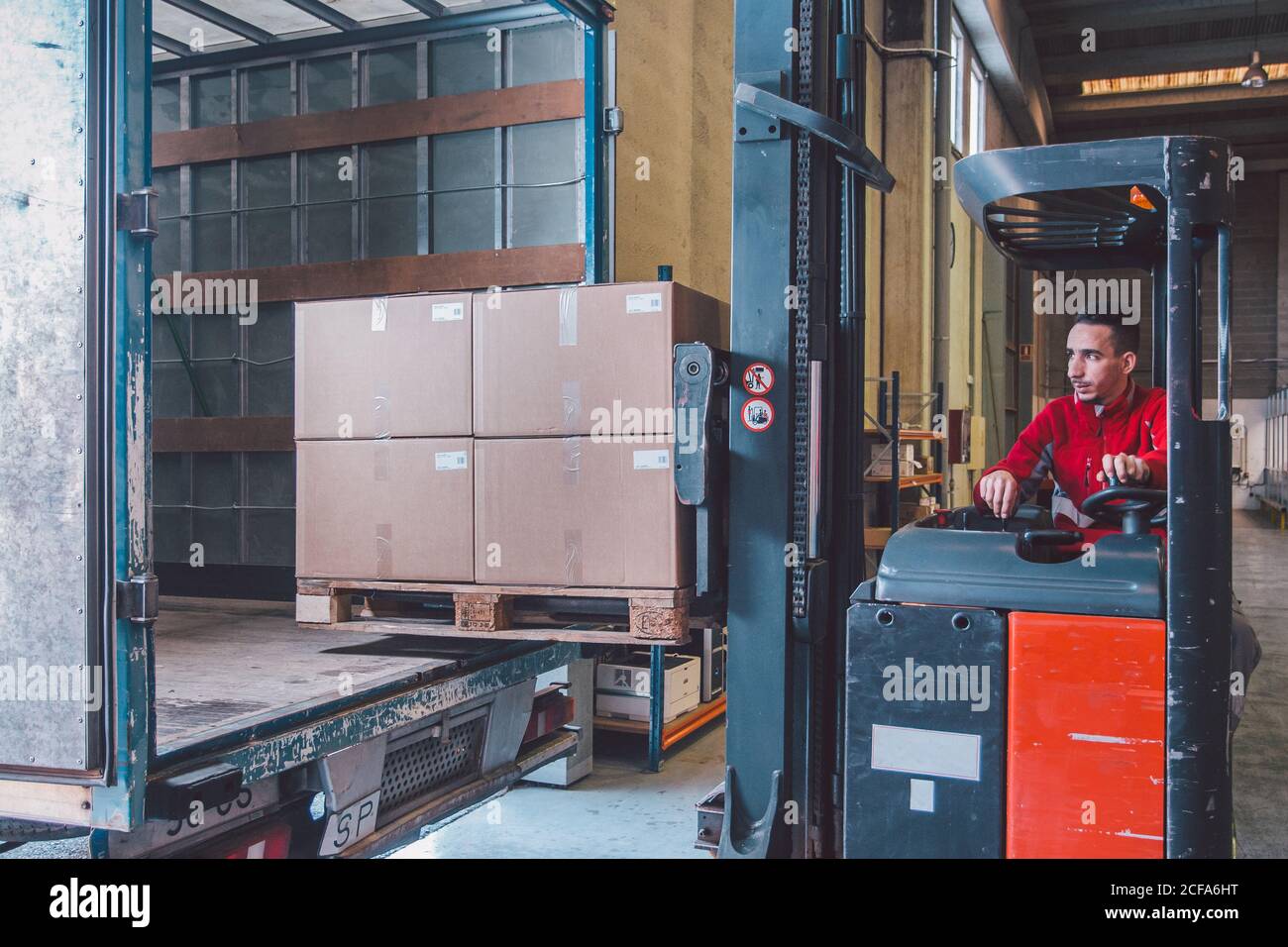Männlicher Fahrer des Gabelstaplers während der Sendung Pakete von groß LKW im modernen Lager Stockfoto