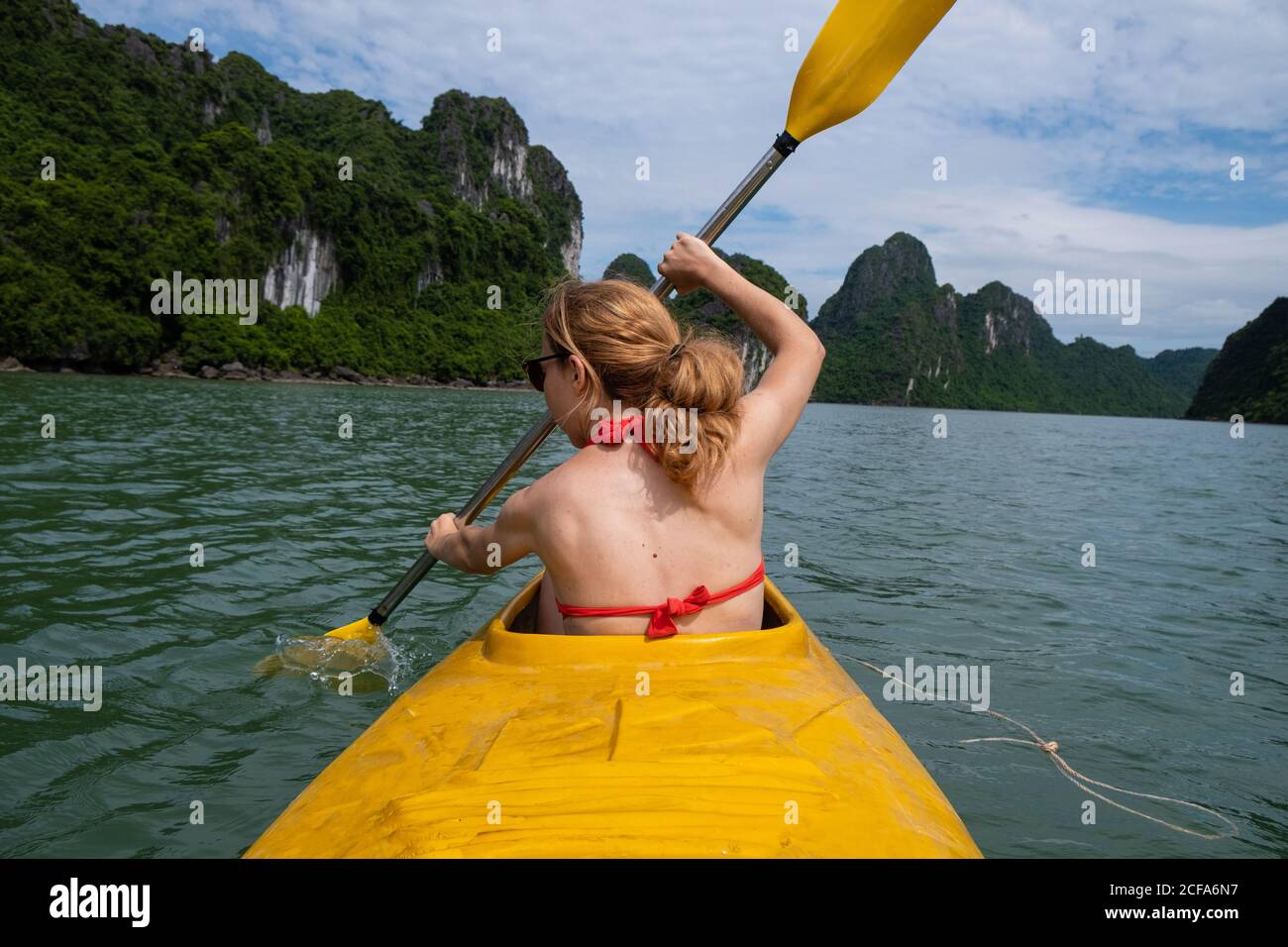 Rückansicht einer nicht erkennbaren Frau im Badeanzug, die im gelben Kanu während des Urlaubs in Vietnam paddelt Stockfoto