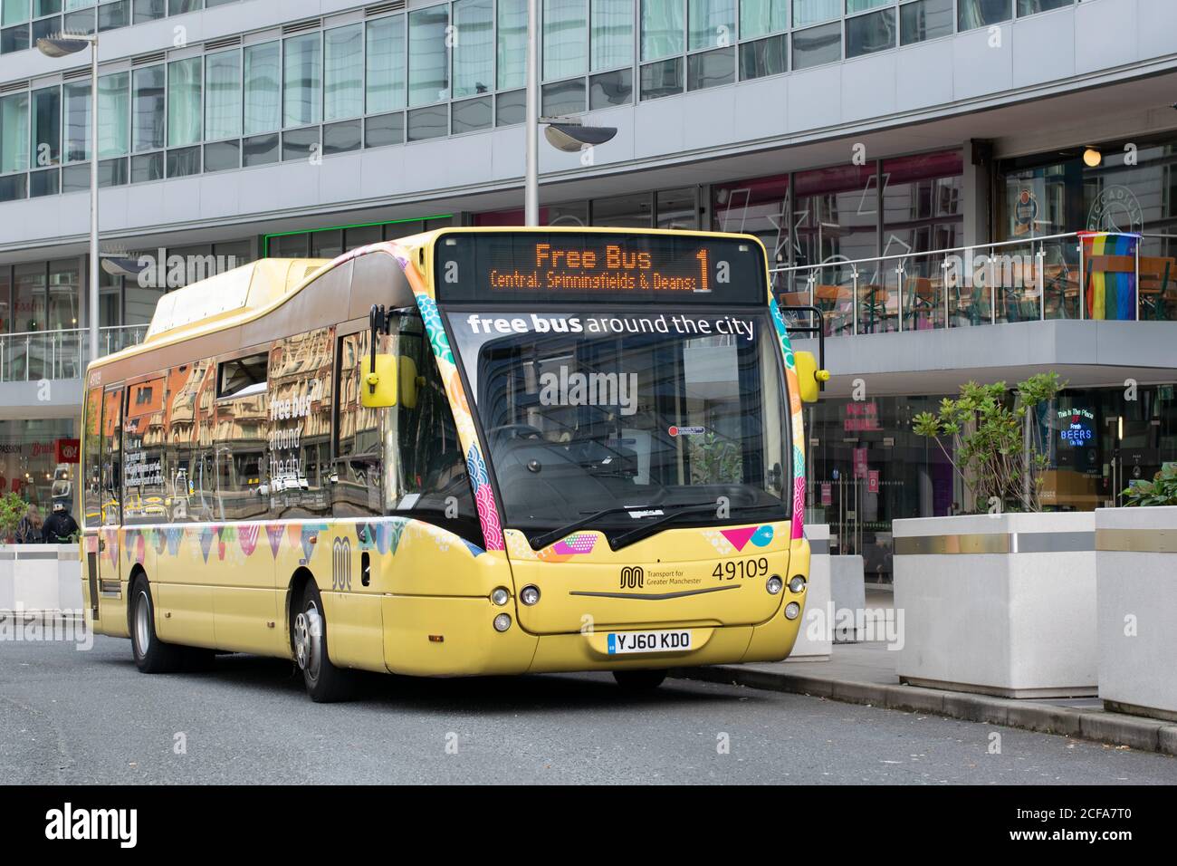 Kostenloser Busservice am Bahnhof Manchester Piccadilly in Großbritannien. Gelber Bus mit geschwungener Fassade des Bürogebäudes im Hintergrund. Elektrischer Diesel-Hybrid. Stockfoto
